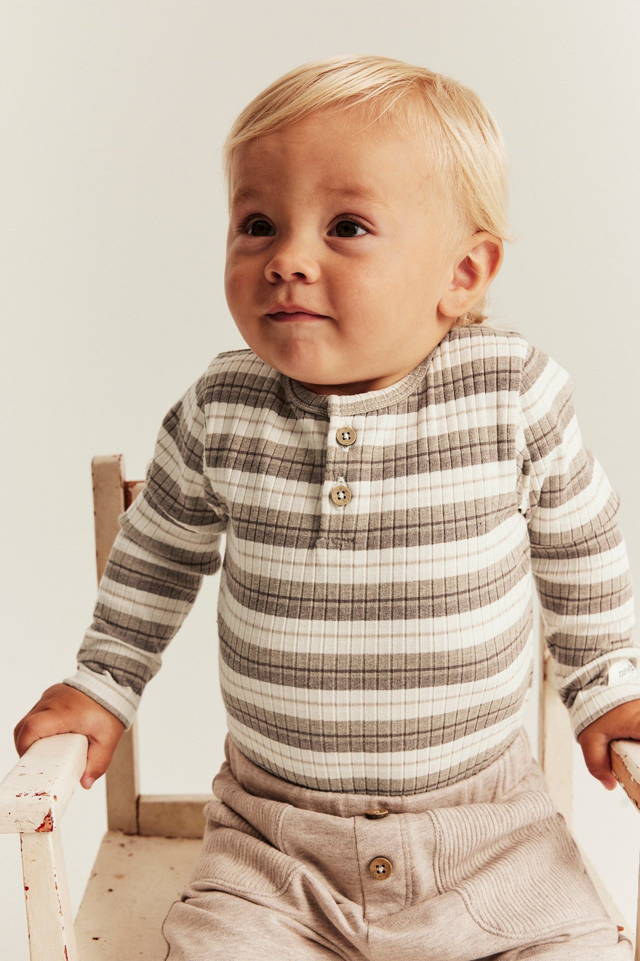 Edestä: vauva raidallisessa ribatussa pitkähihaisessa bodyssä napeilla ja vaaleanbeigessä ribatussa housussa.
