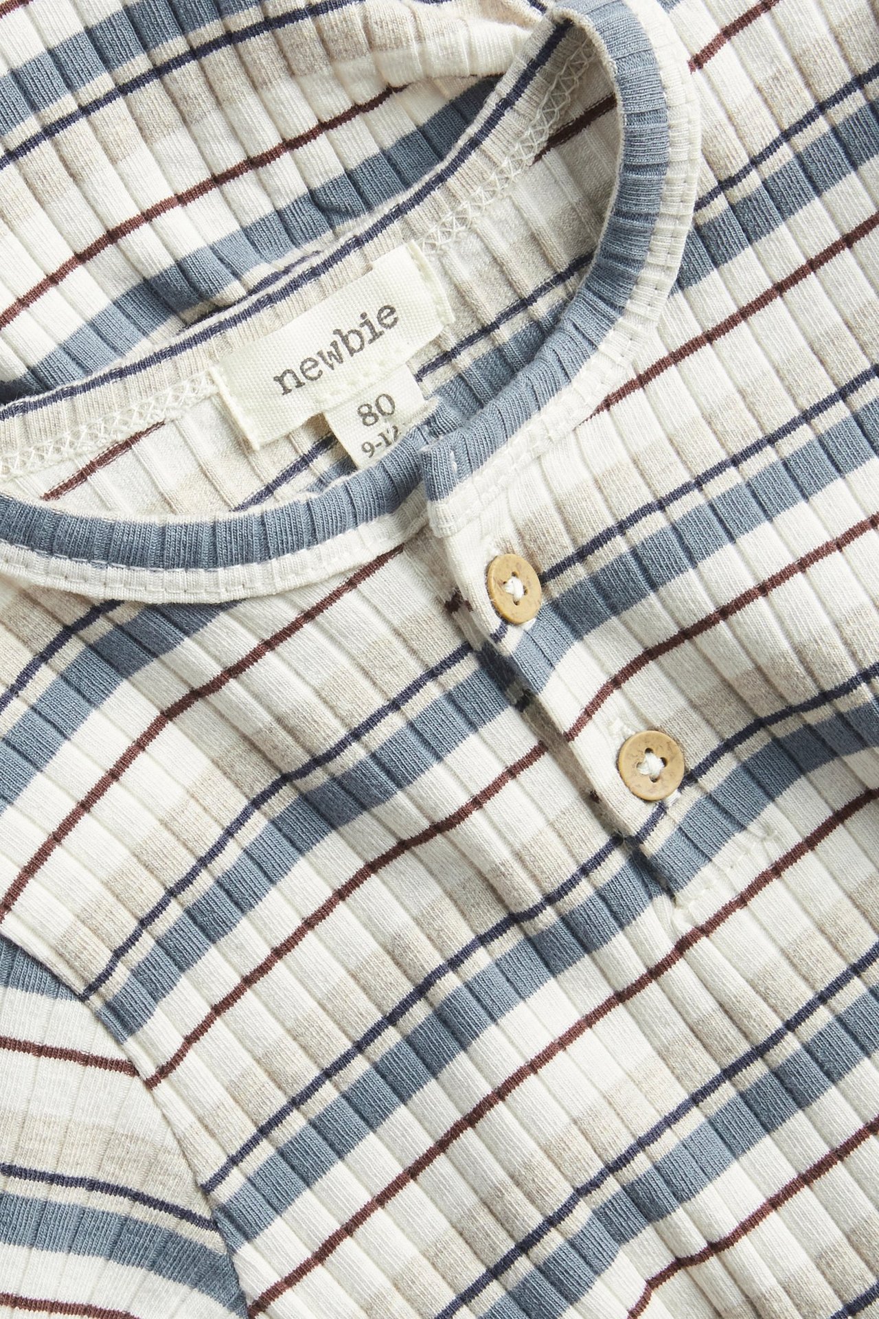 Zbliżenie na prążkowane, długie body niemowlęce w niebieskie, beżowe i brązowe paski, z guzikami z przodu.