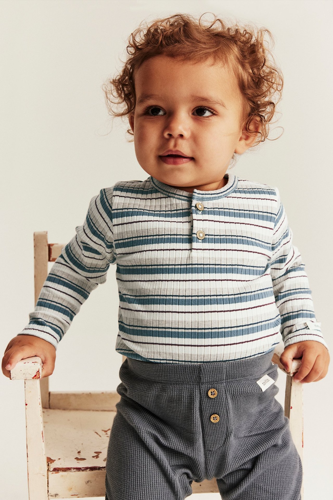 Edestäpäin: vauva siniraitaisessa pitkähihaisessa ribbibodyssä ja tummanharmaissa vohvelihousuissa.