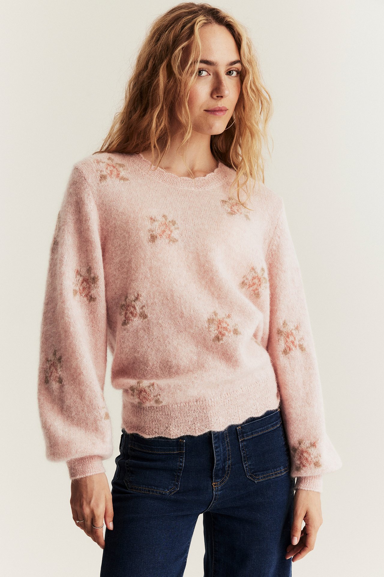 Frontbilde av kvinne i rosa blomstret mohair- og ullblanding genser og mørkeblå jeans.