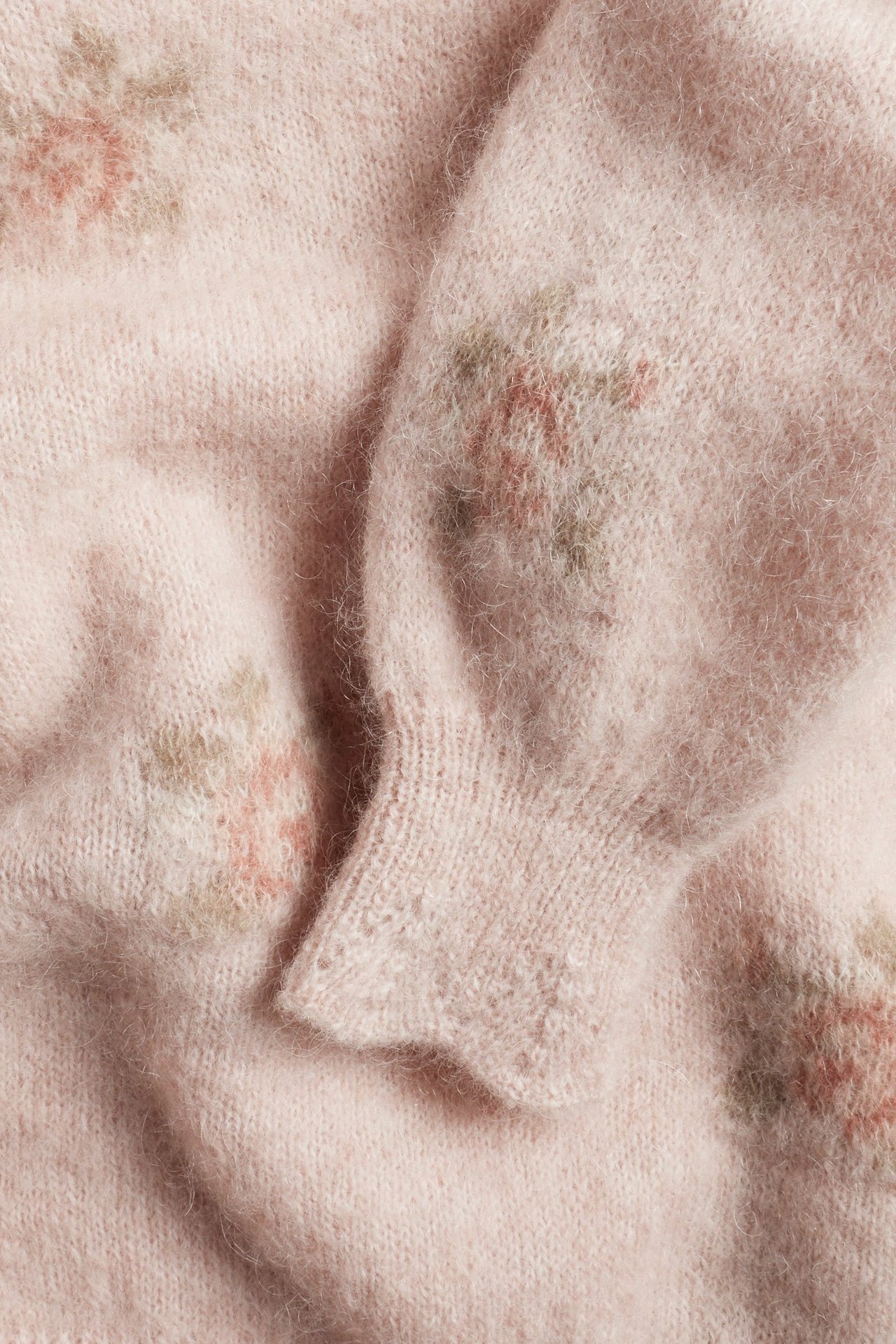 Zbliżenie różowego swetra z mieszanki wełny z żakardowym wzorem w róże i ściągaczami z koronkową krawędzią.