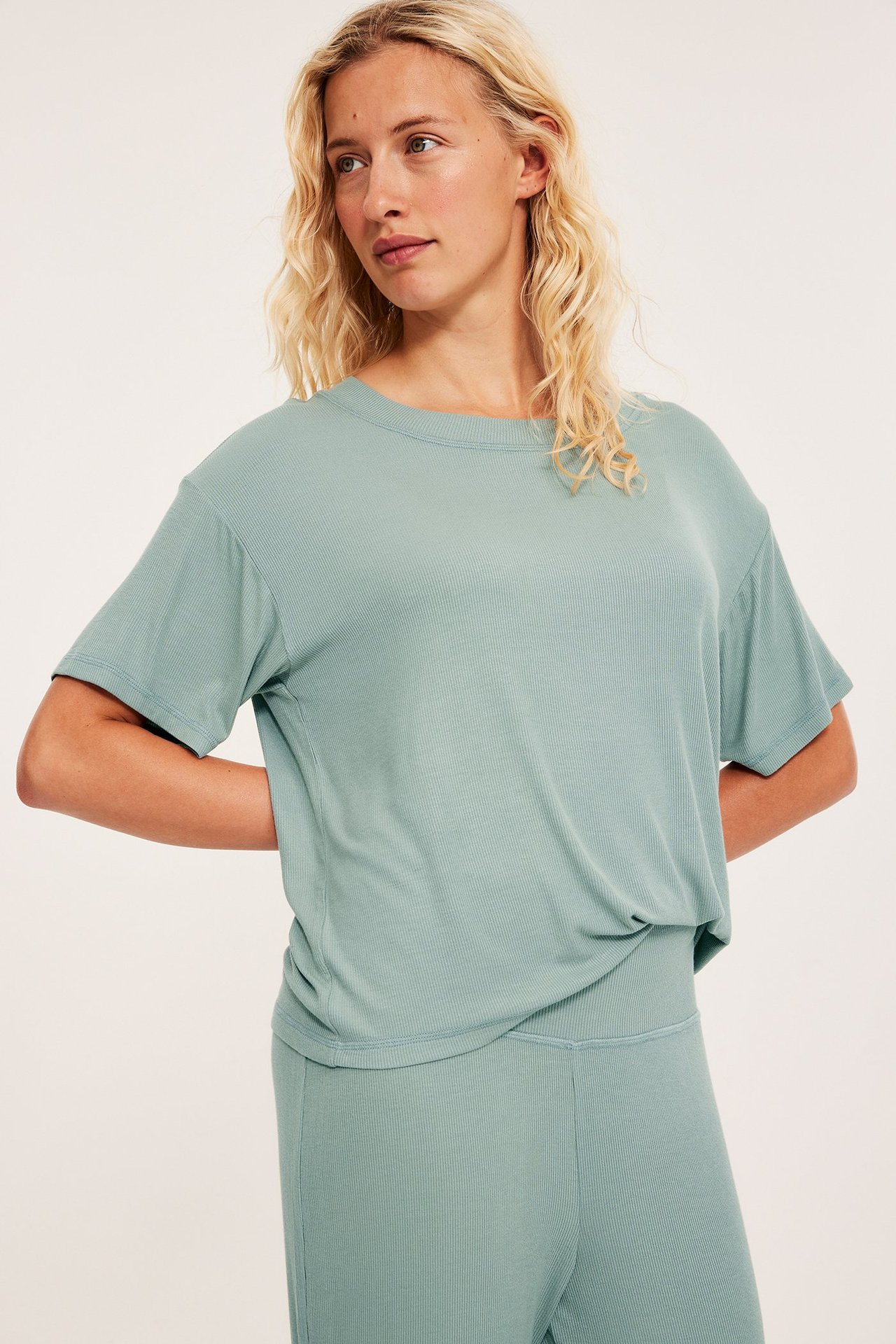 Edestä kuvattu nainen yllään vaaleanvihreä ribattu pyjamatoppi ja yhteensopivat ribatut pyjamahousut.