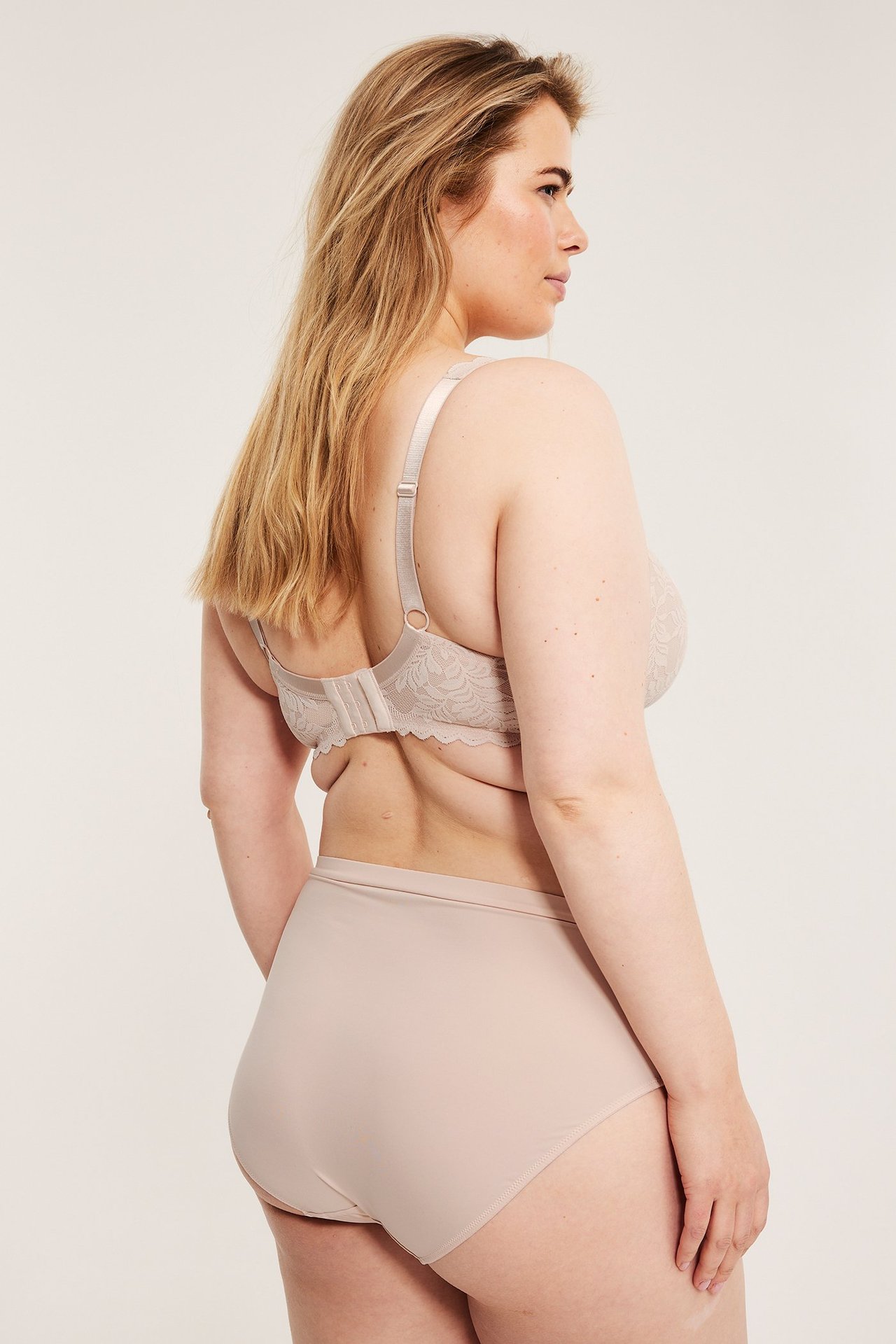 Widok z tyłu kobiety w jasnoróżowym, wyściełanym biustonoszu koronkowym i pasujących majtkach.