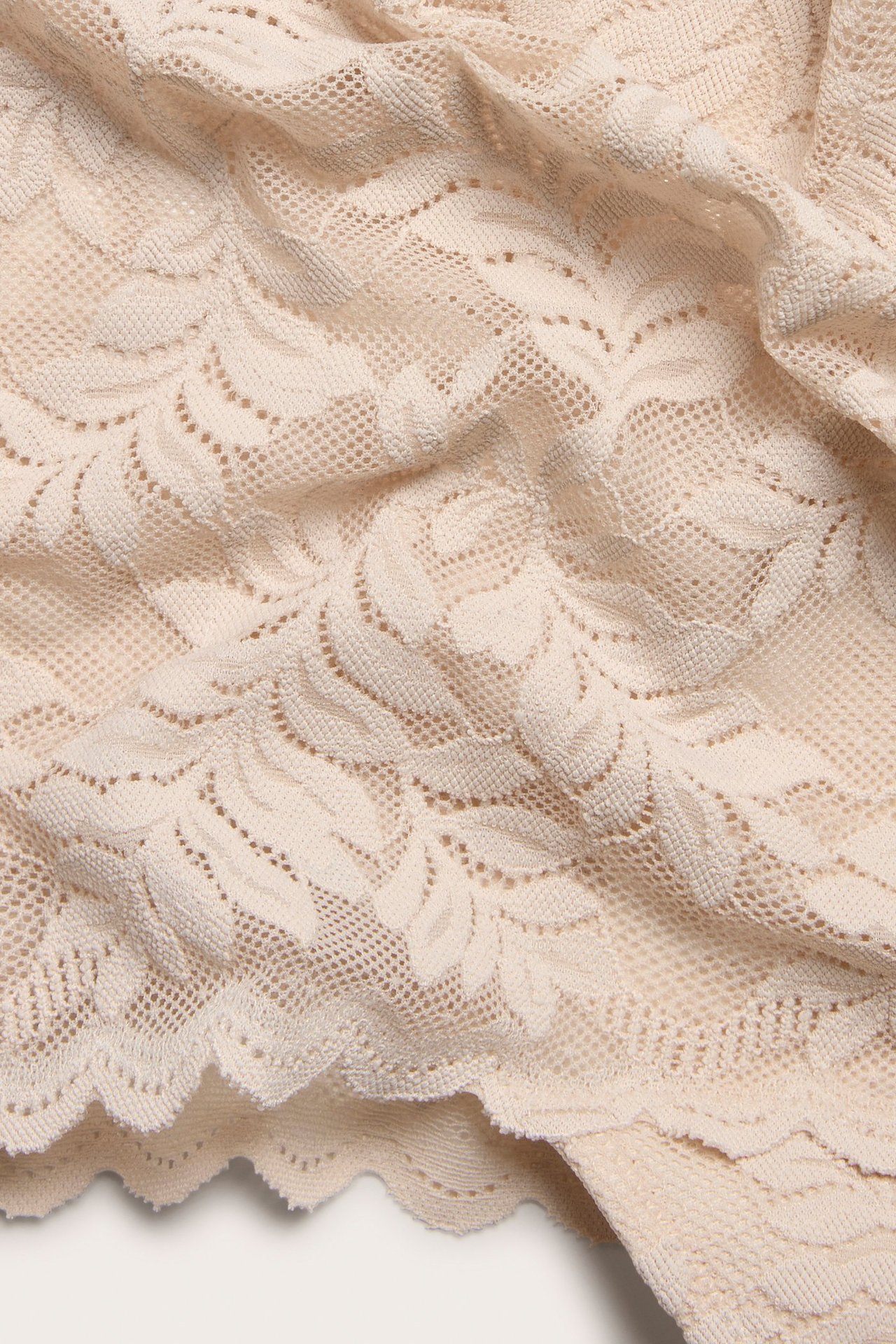 Zbliżenie jasnoróżowych koronkowych stringów z wysokim stanem, ukazujące szczegółowy wzór kwiatowy.