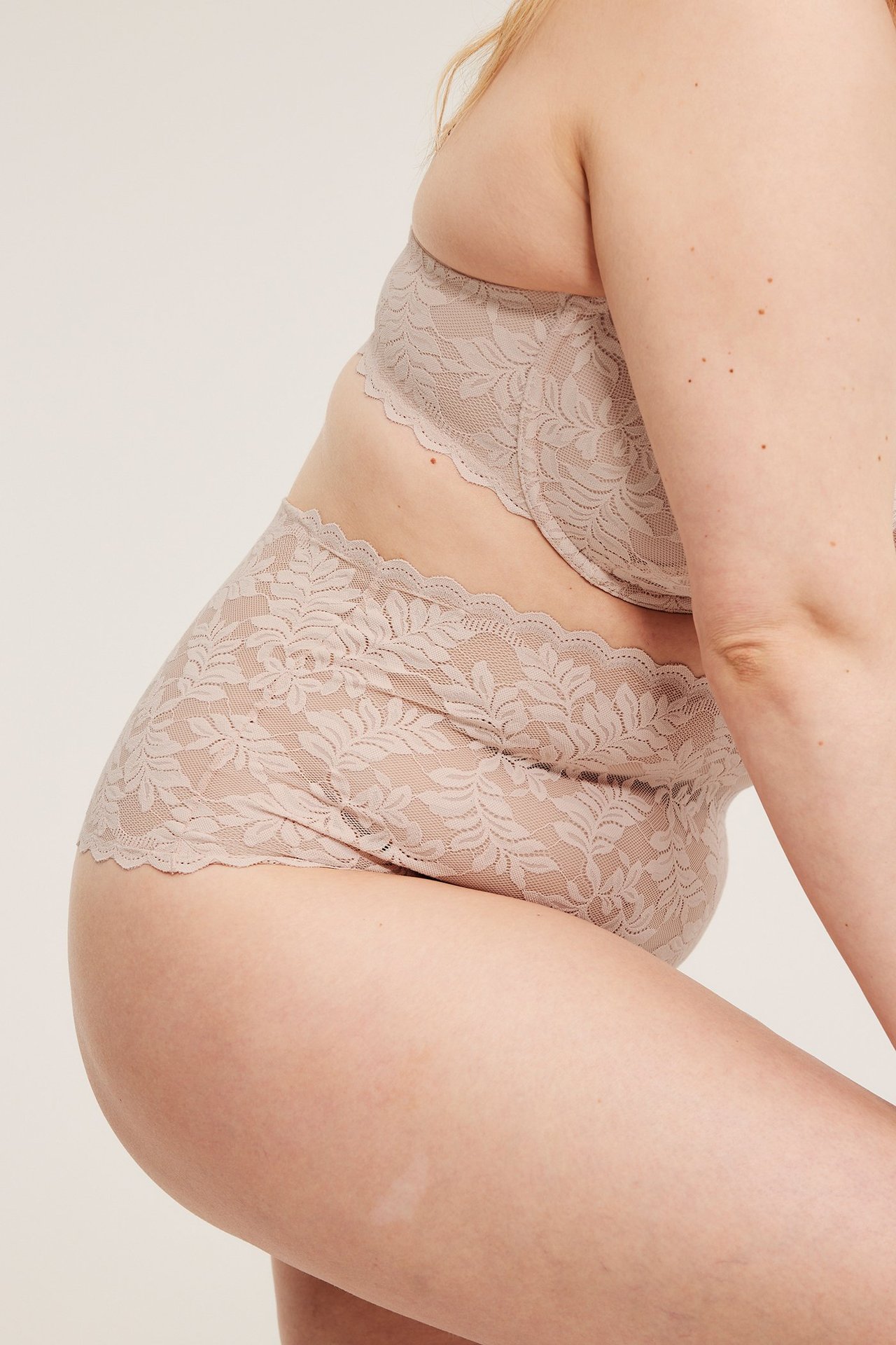 Widok z boku kobiety w jasnoróżowych koronkowych figach z wysokim stanem i pasującym biustonoszu.