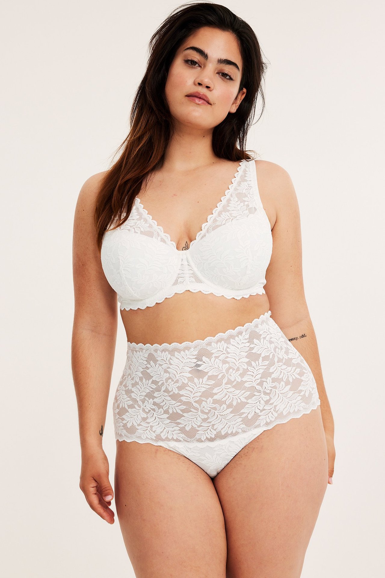 Frontvy av kvinna i offwhite hög midja spetstrosa och matchande spets-bh.