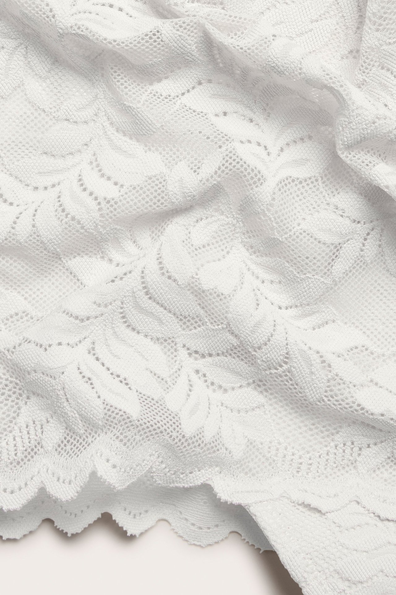 Zbliżenie na ecru koronkowe figi z wysokim stanem i kwiatowym wzorem.