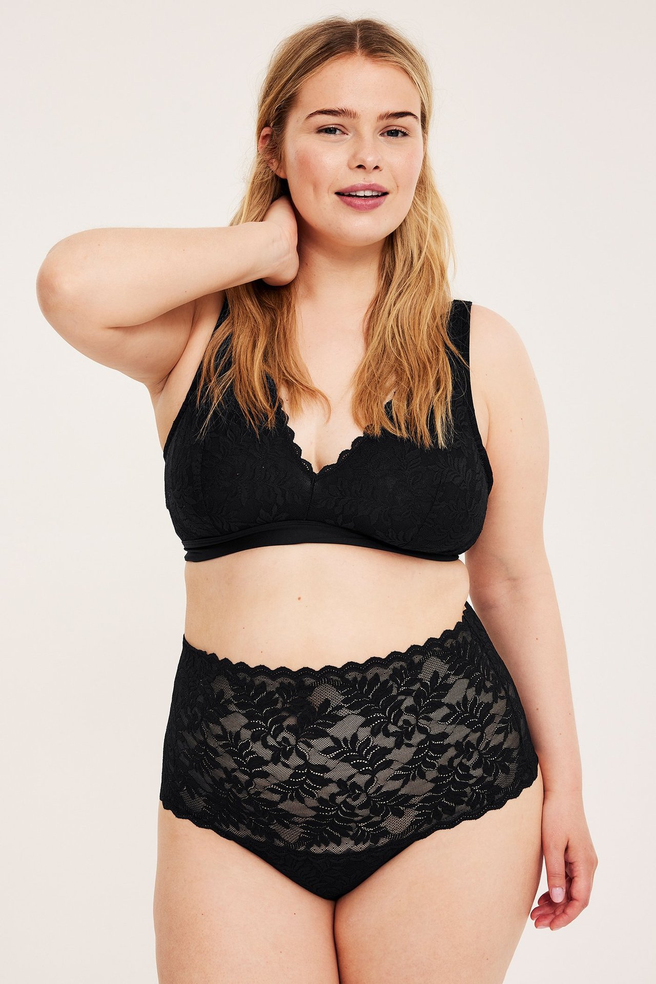 Widok z przodu kobiety w czarnych koronkowych figach z wysokim stanem i pasującym koronkowym biustonoszu.
