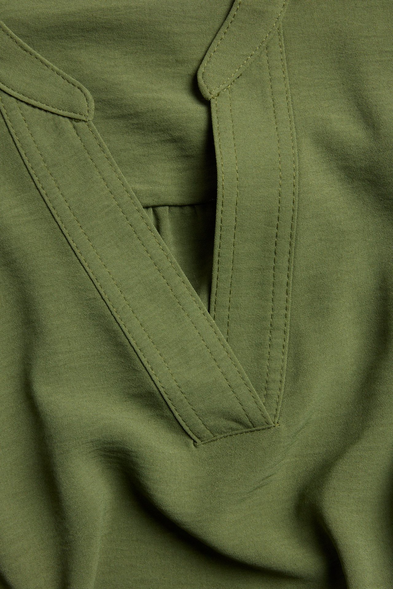 Zbliżenie na ciemnozieloną bluzkę poliestrową z dekoltem w serek, bez zapięcia z przodu.