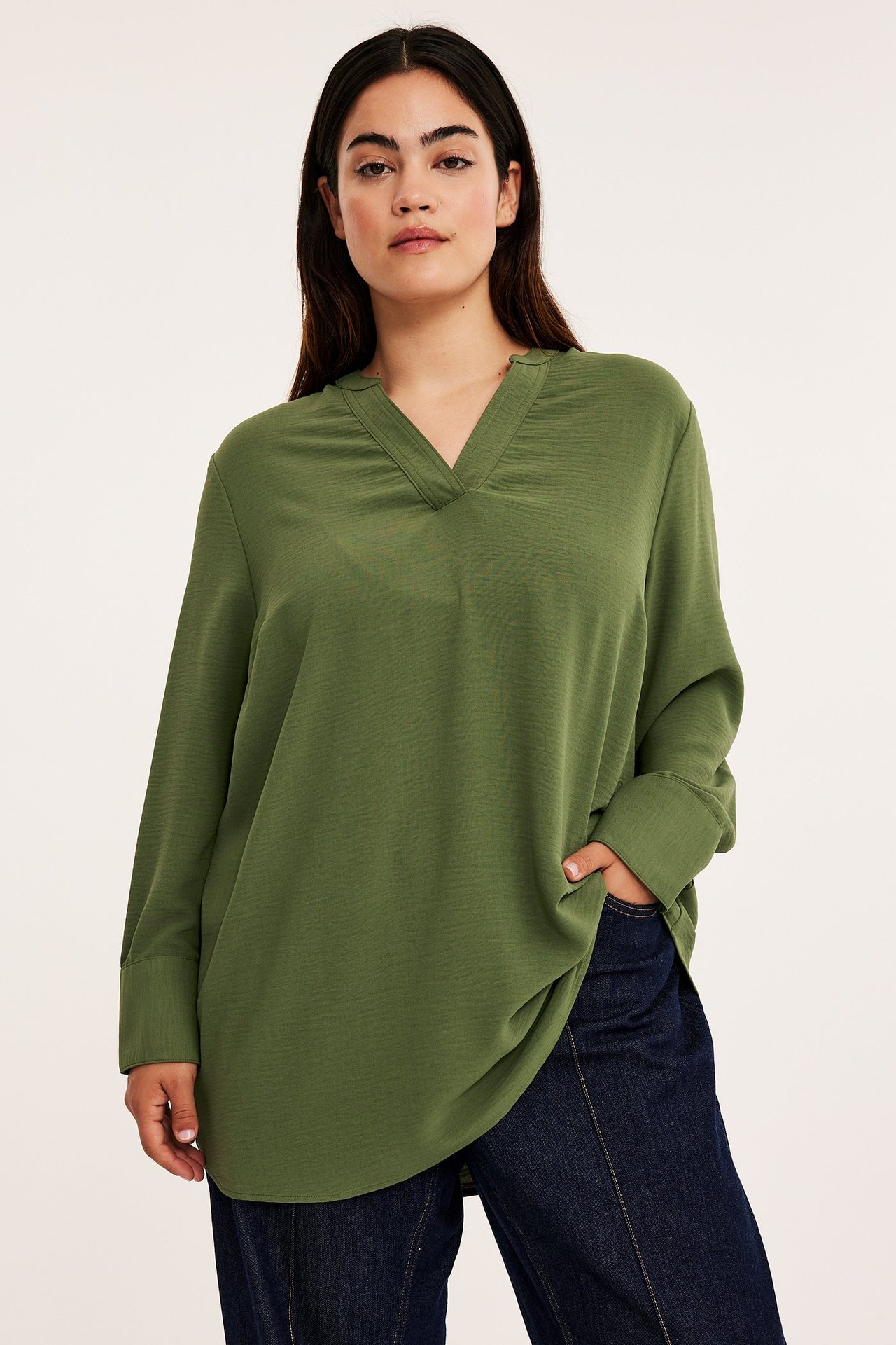 Widok z przodu kobiety w ciemnozielonej bluzce poliestrowej z dekoltem w serek i ciemnoniebieskich dżinsach.