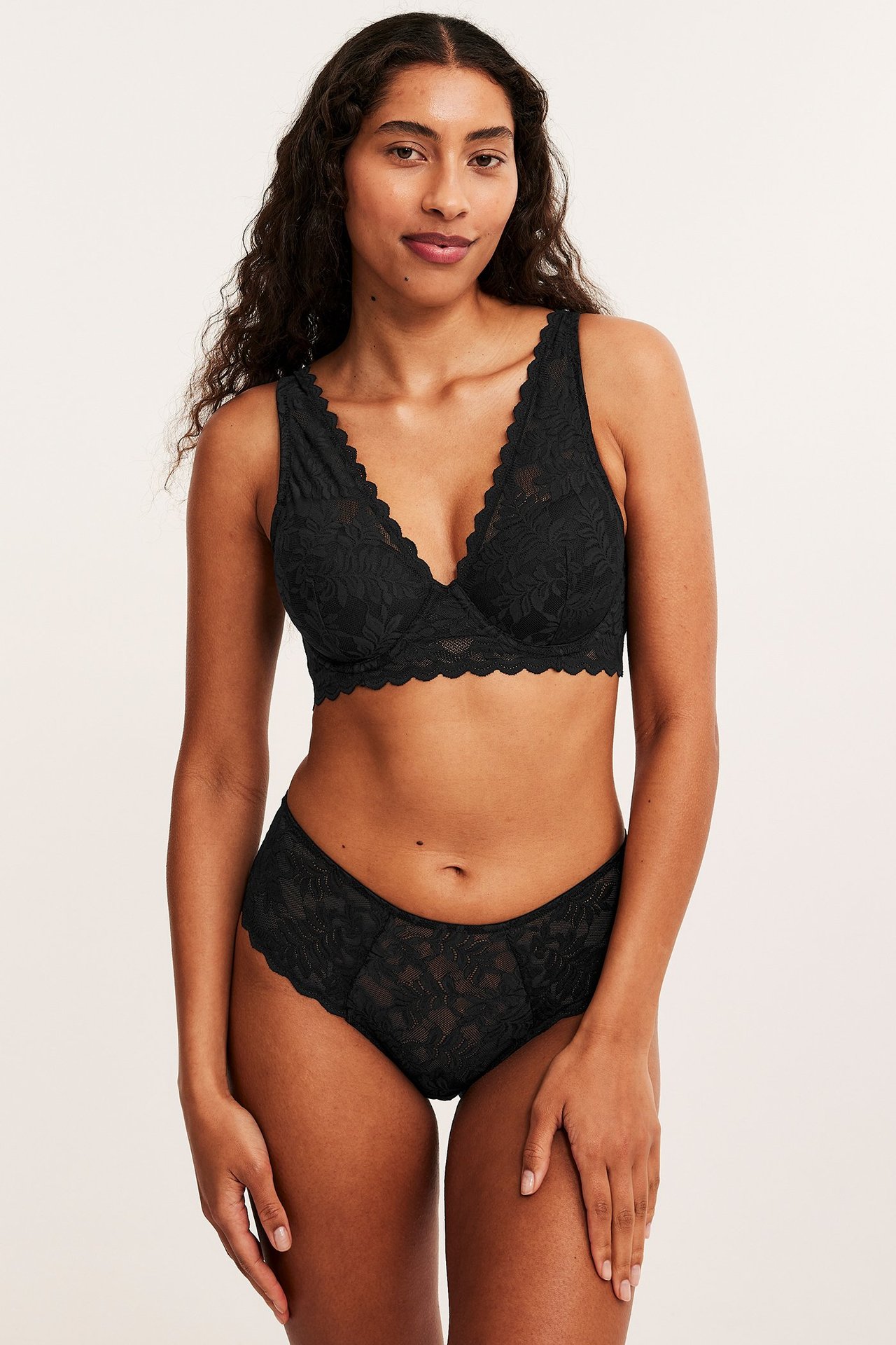 Frontbilde av en kvinne i svarte blonde mid-brief truser og en matchende svart blondebralette.