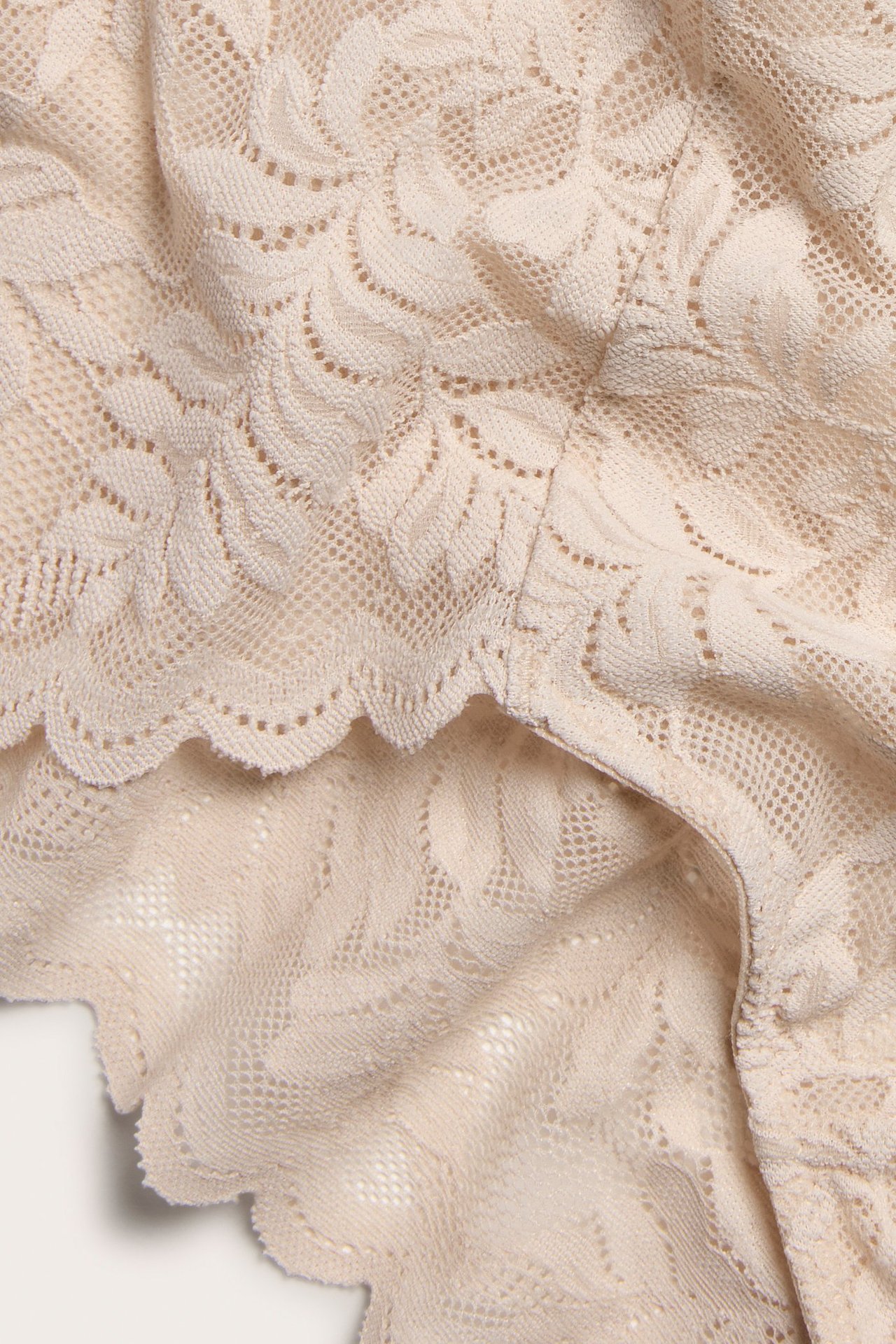 Zbliżenie jasnoróżowych koronkowych majtek typu brief z kwiatowym wzorem i falistym brzegiem.