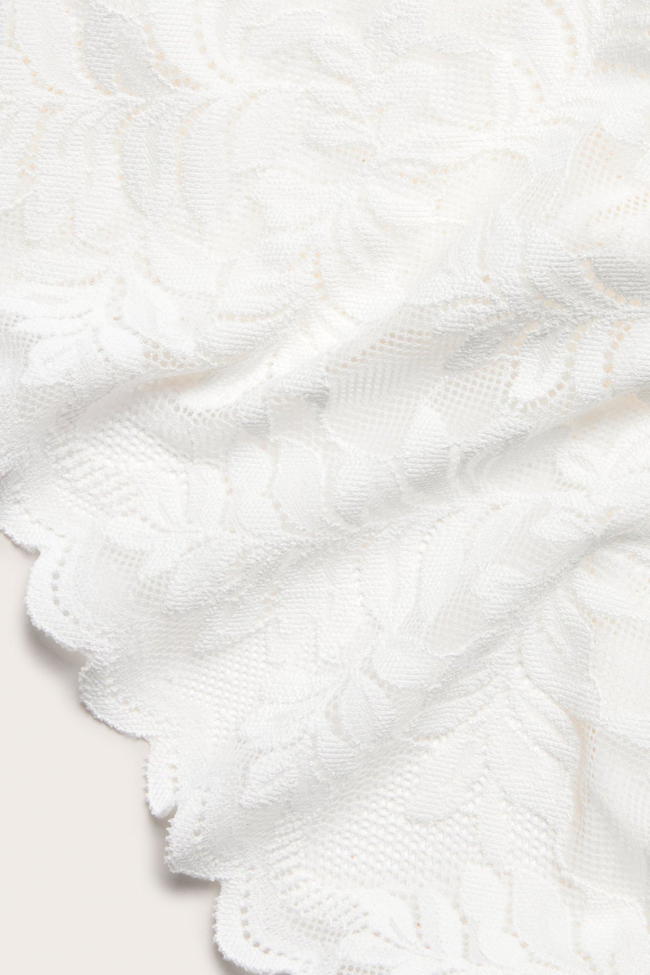 Zbliżenie na ecru koronkowy materiał majtek typu brief z falistym brzegiem.