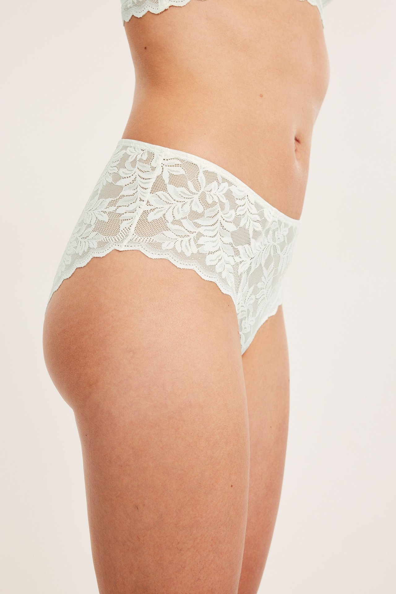 Sidebilde av kvinne i offwhite blonde mid-brief truser med blomstermønster og matchende BH.