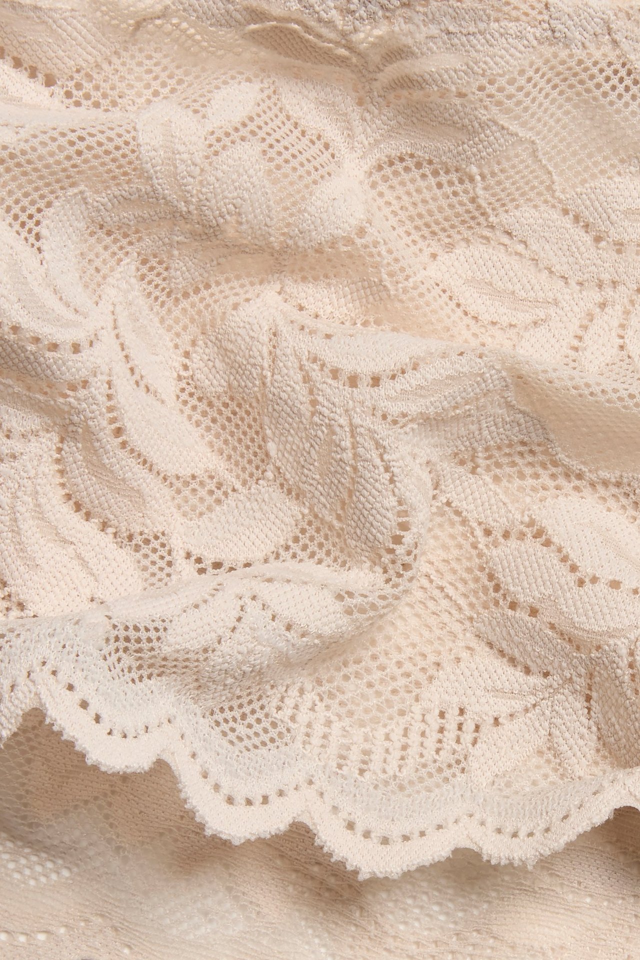 Zbliżenie jasnoróżowych koronkowych stringów z delikatnym wzorem liści.