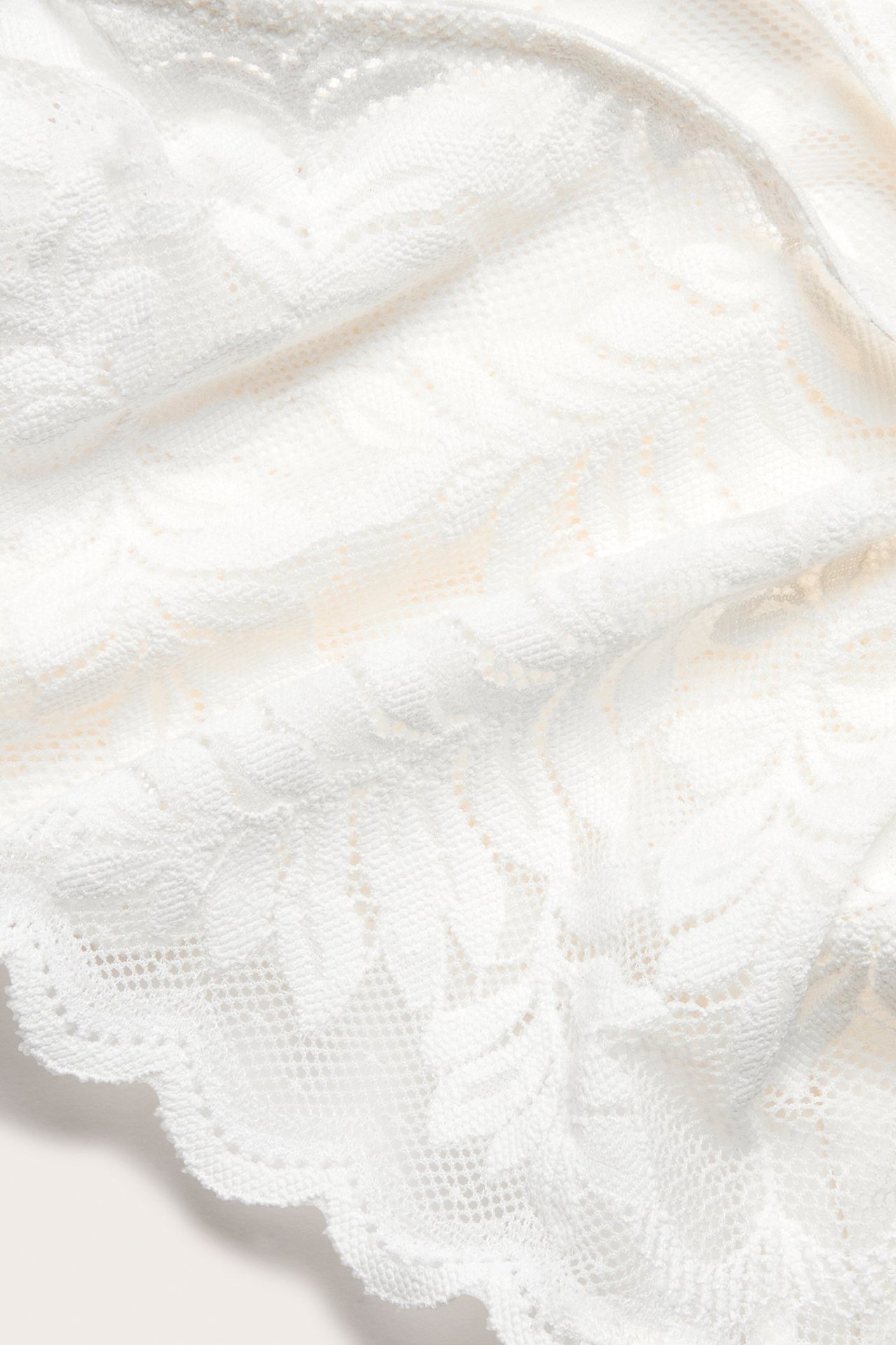 Zbliżenie na ecru koronkowy materiał stringów z kwiatowym wzorem i falistym brzegiem.