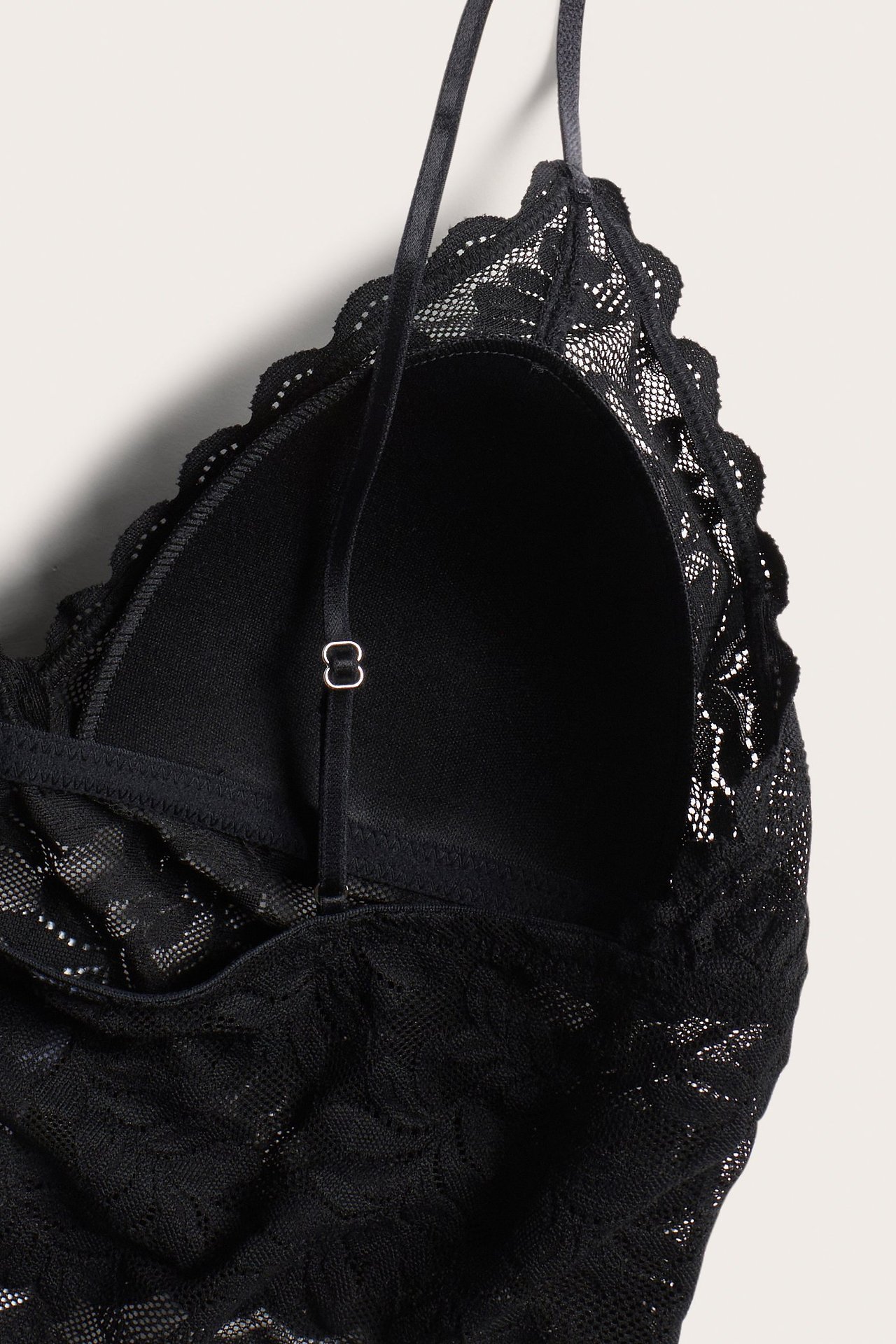 Zbliżenie czarnego koronkowego biustonosza z wbudowaną wyściółką, falistym brzegiem i regulowanym ramiączkiem.