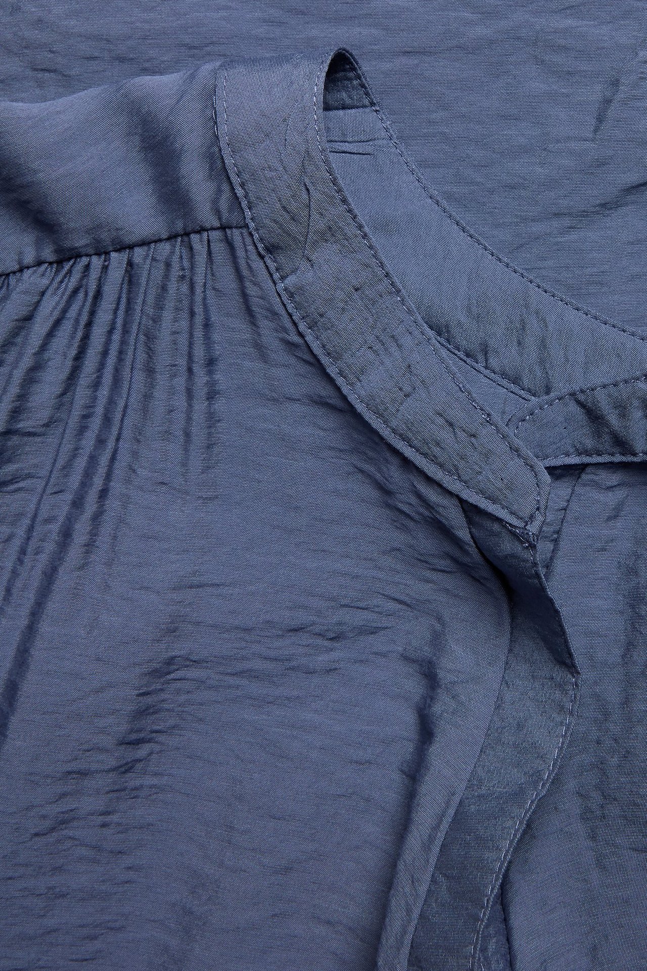 Zbliżenie niebieskiej, strukturalnej bluzki z kołnierzykowym dekoltem i marszczonym materiałem.