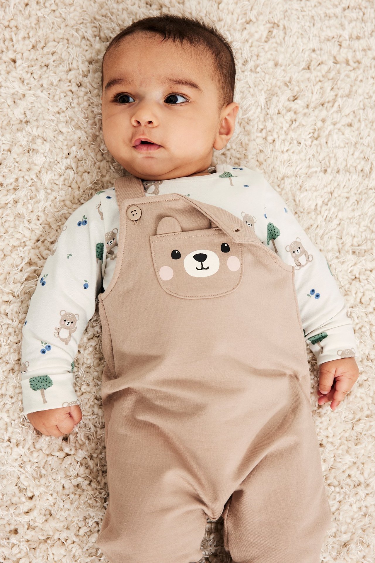 Edestäpäin: vauva yllään beiget haalarit karhun kasvoilla taskussa, alla luonnonvalkoinen karhukuvioinen body.