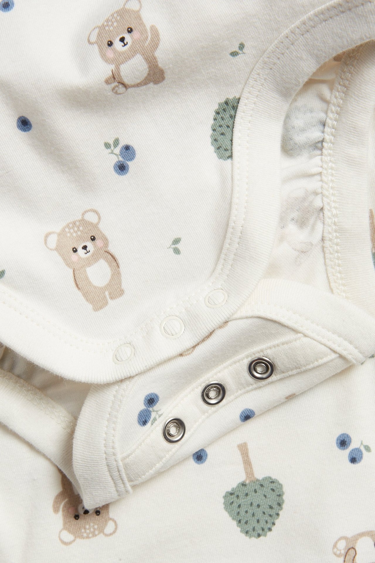 Zbliżenie na ecru body niemowlęce z nadrukiem niedźwiedzi i jagód, zapinane na zatrzaski.
