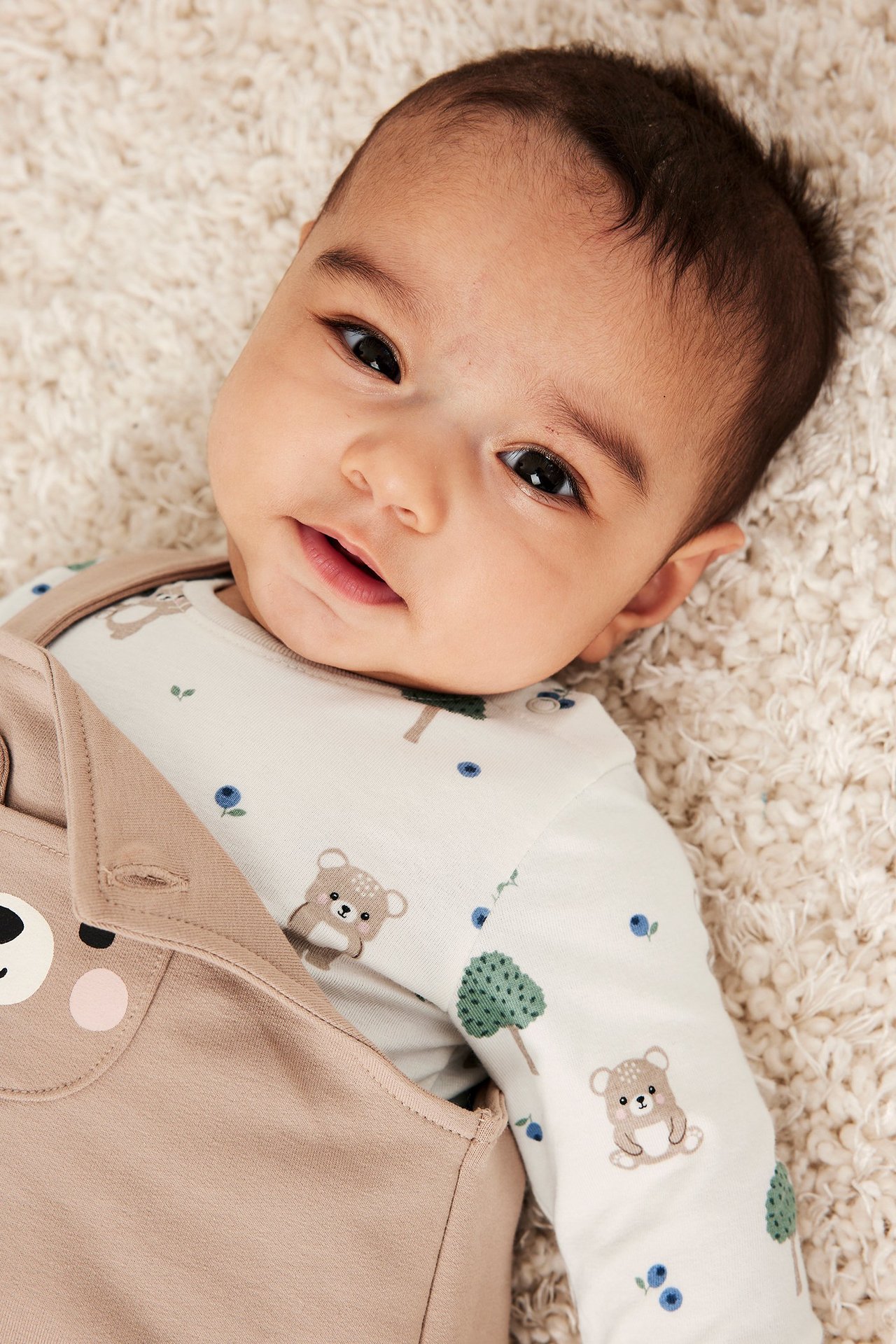 Lähikuva vauvasta yllään luonnonvalkoinen pitkähihainen body karhukuviolla, vaaleanruskean haalarin alla.