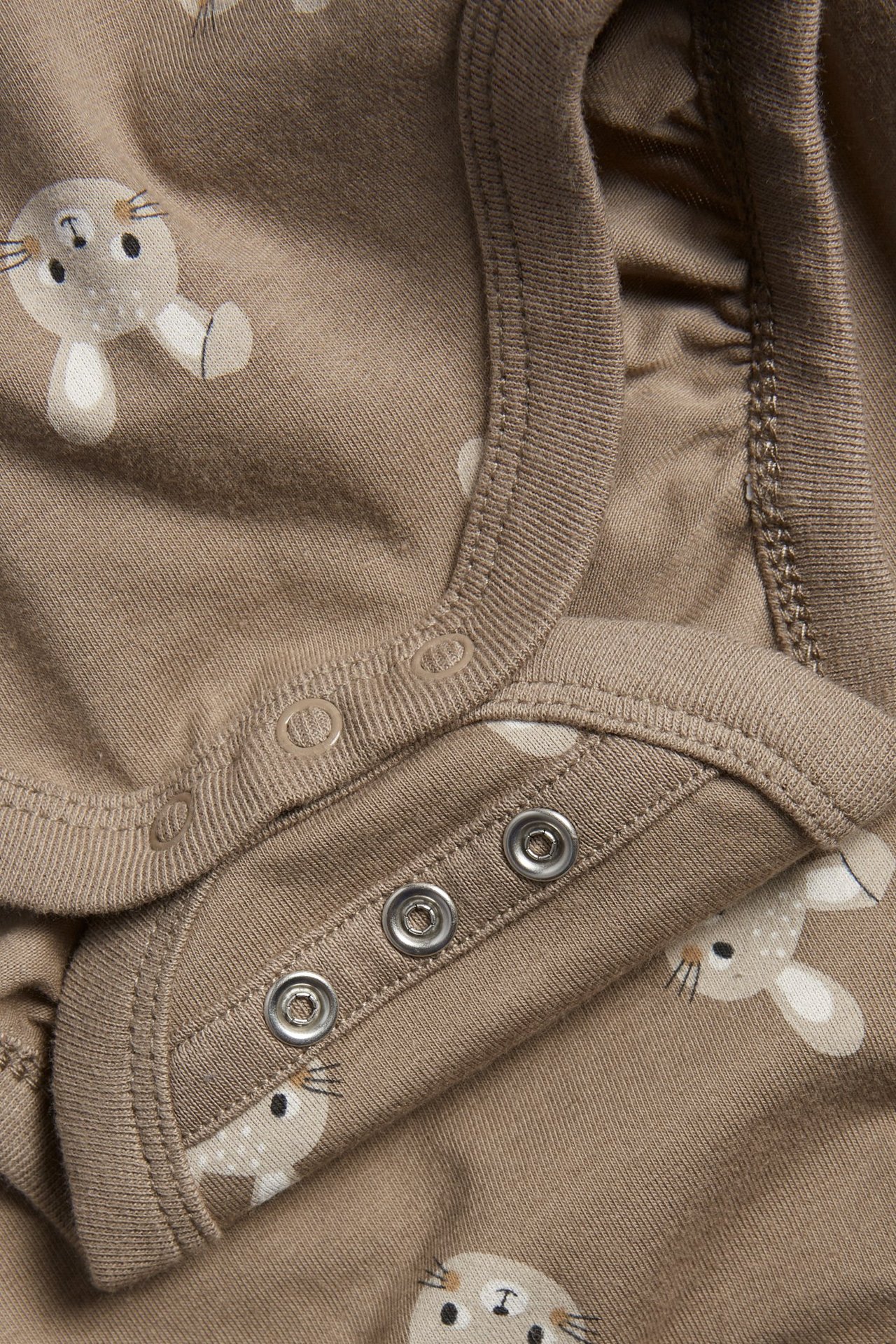 Zbliżenie na brązowe body niemowlęce z wzorem w króliczki i zatrzaskami.