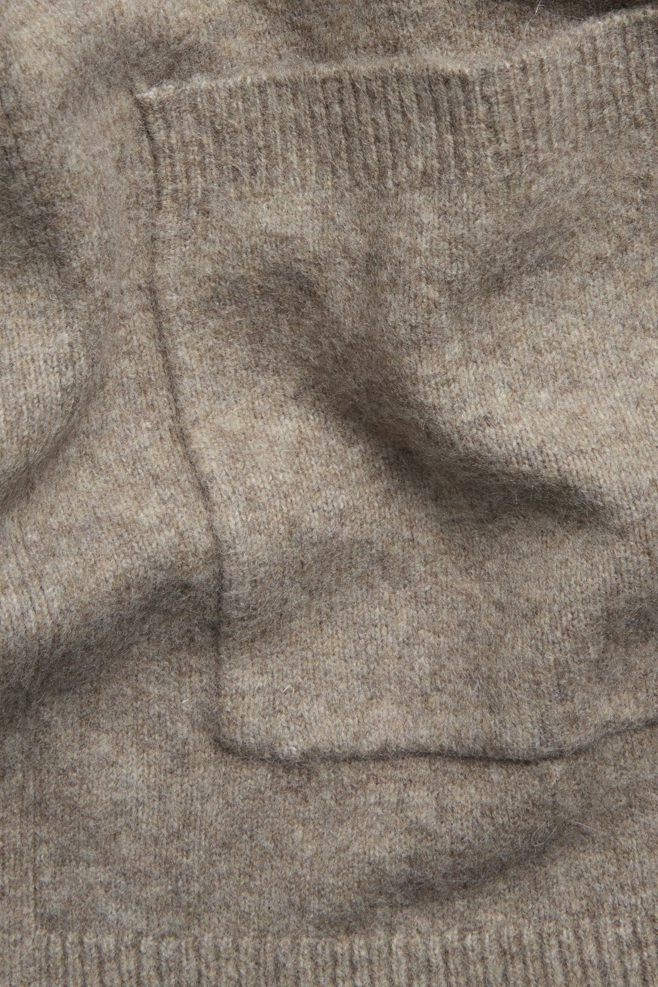 Zbliżenie beżowego melanżowego długiego kardiganu z widoczną kieszenią.