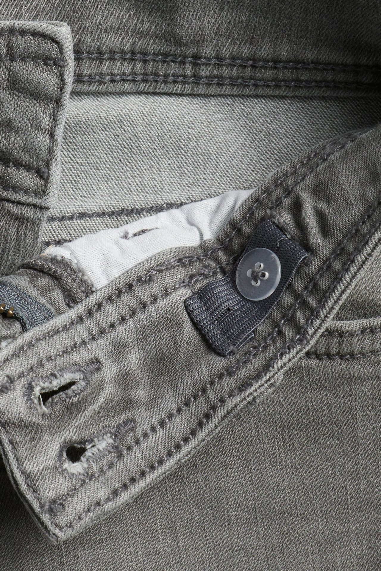 Zbliżenie na szare jeansy bootcut z denimu, pokazujące regulowaną talię z guzikiem i gumką.