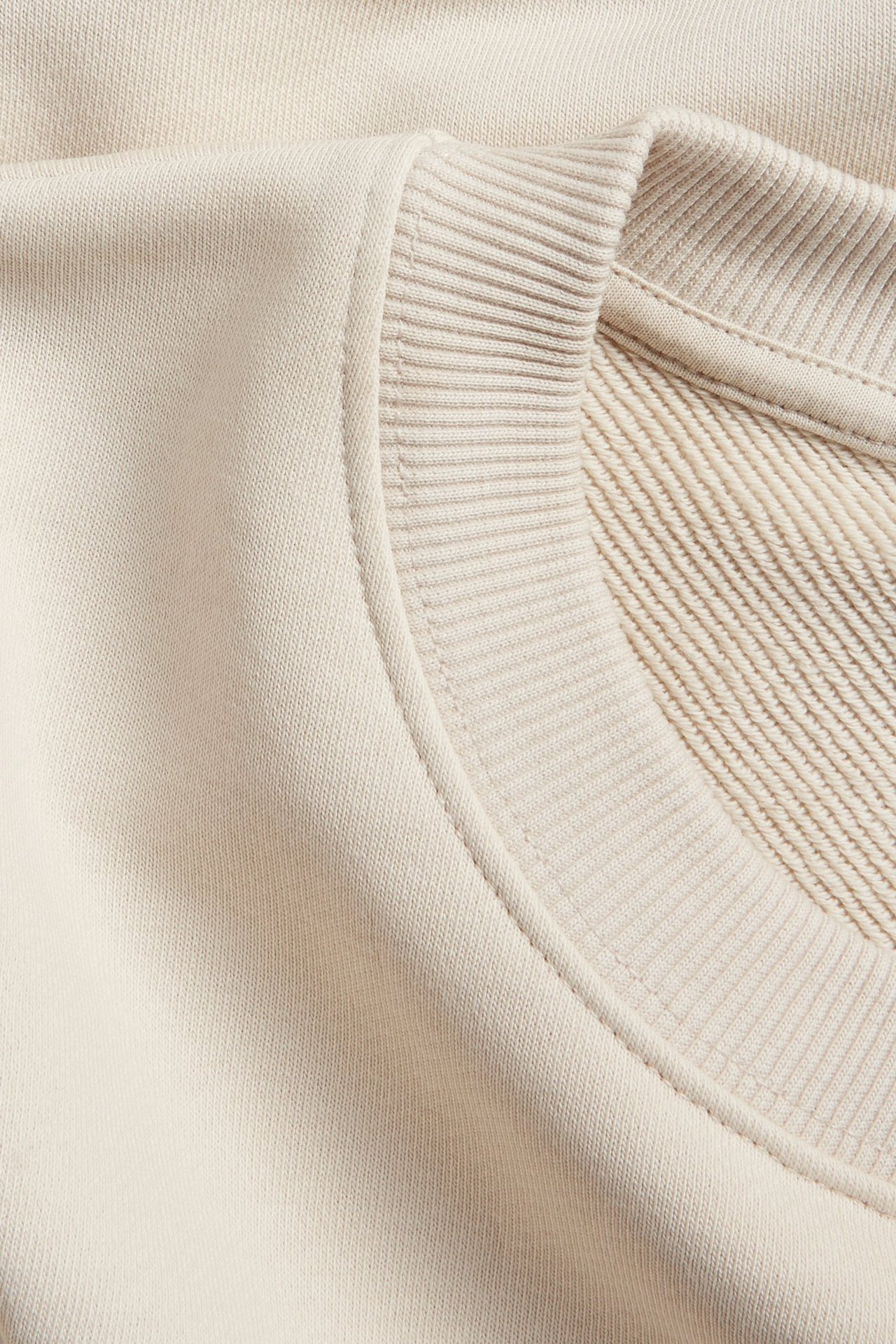 Zbliżenie na jasnobeżową bluzę oversize z prążkowanym okrągłym dekoltem i obniżoną linią ramion.
