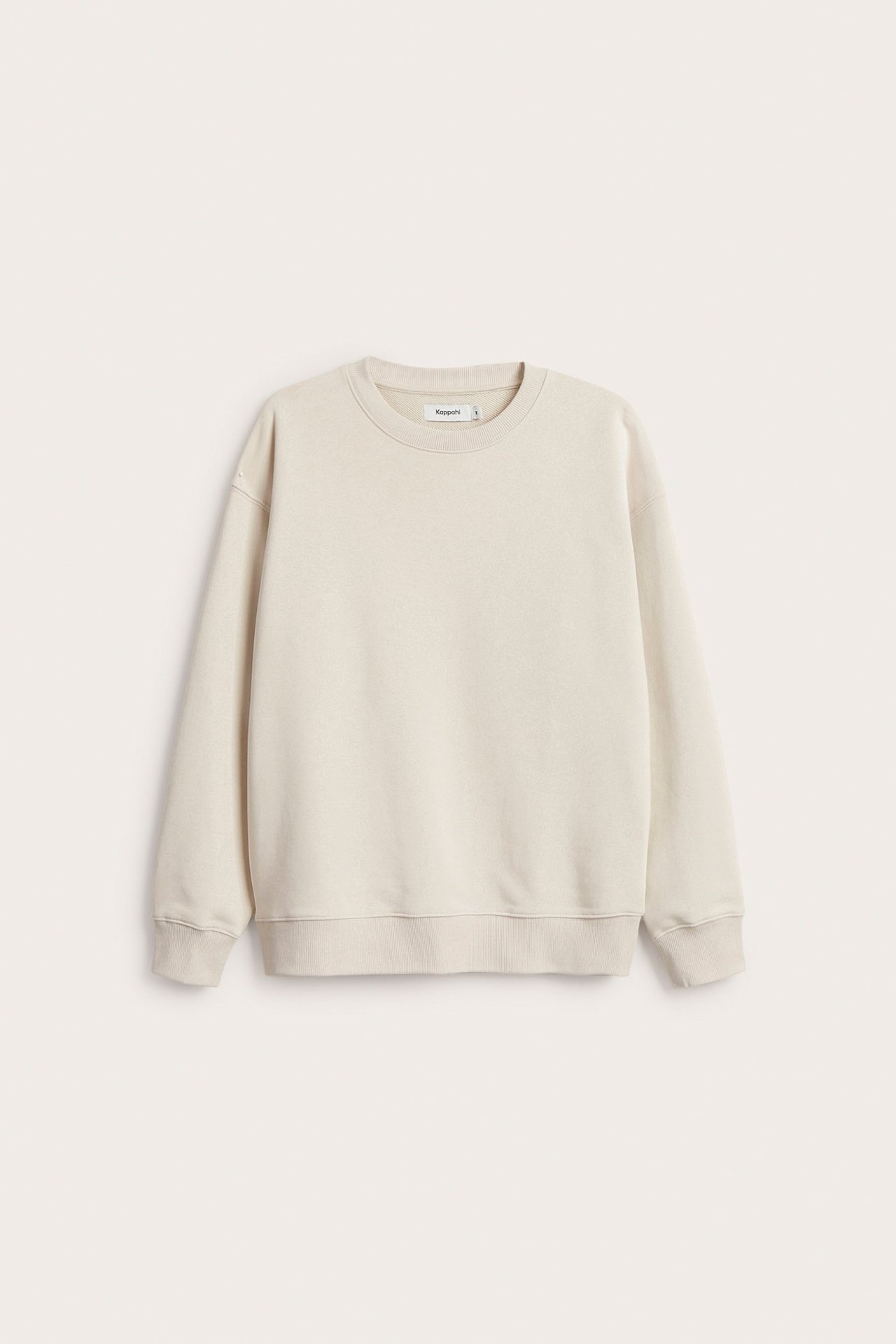 Edestä kuvattu vaaleanbeige oversized puuvillasekoitepusero, jossa on pudotetut olkapäät ja pyöreä pääntie.