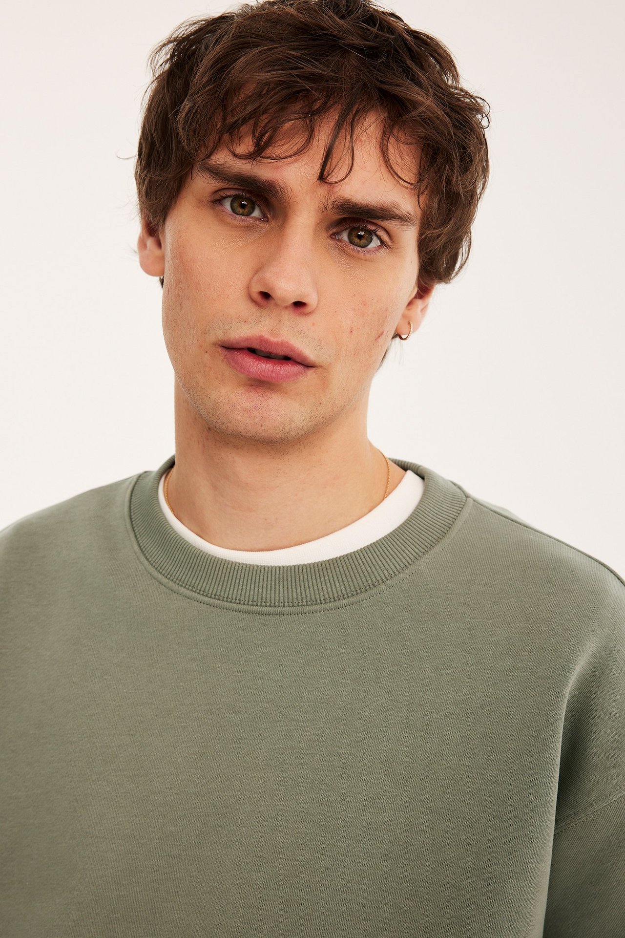 Lähikuva miehestä vihreässä ylisuuressa collegepaidassa valkoisen t-paidan päällä.