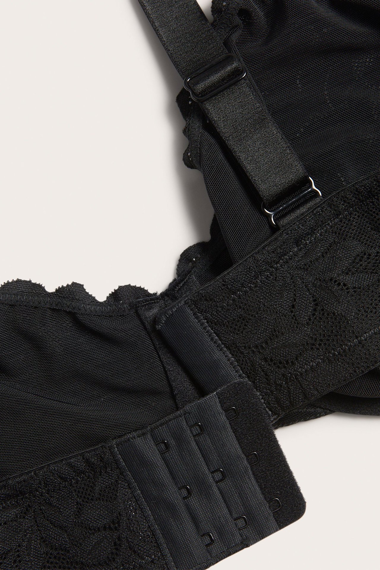 Zbliżenie czarnego biustonosza z fiszbinami, koronkowego, z regulowanymi ramiączkami i zapięciem na haftki.