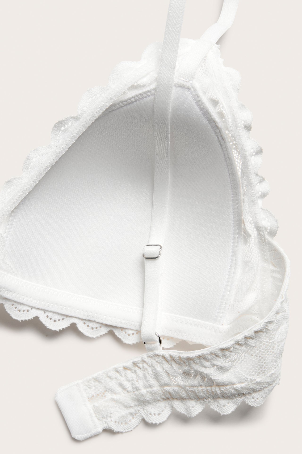 Zbliżenie na ecru koronkowy biustonosz bez fiszbin z regulowanymi ramiączkami, falistymi brzegami i miękkim wypełnieniem.