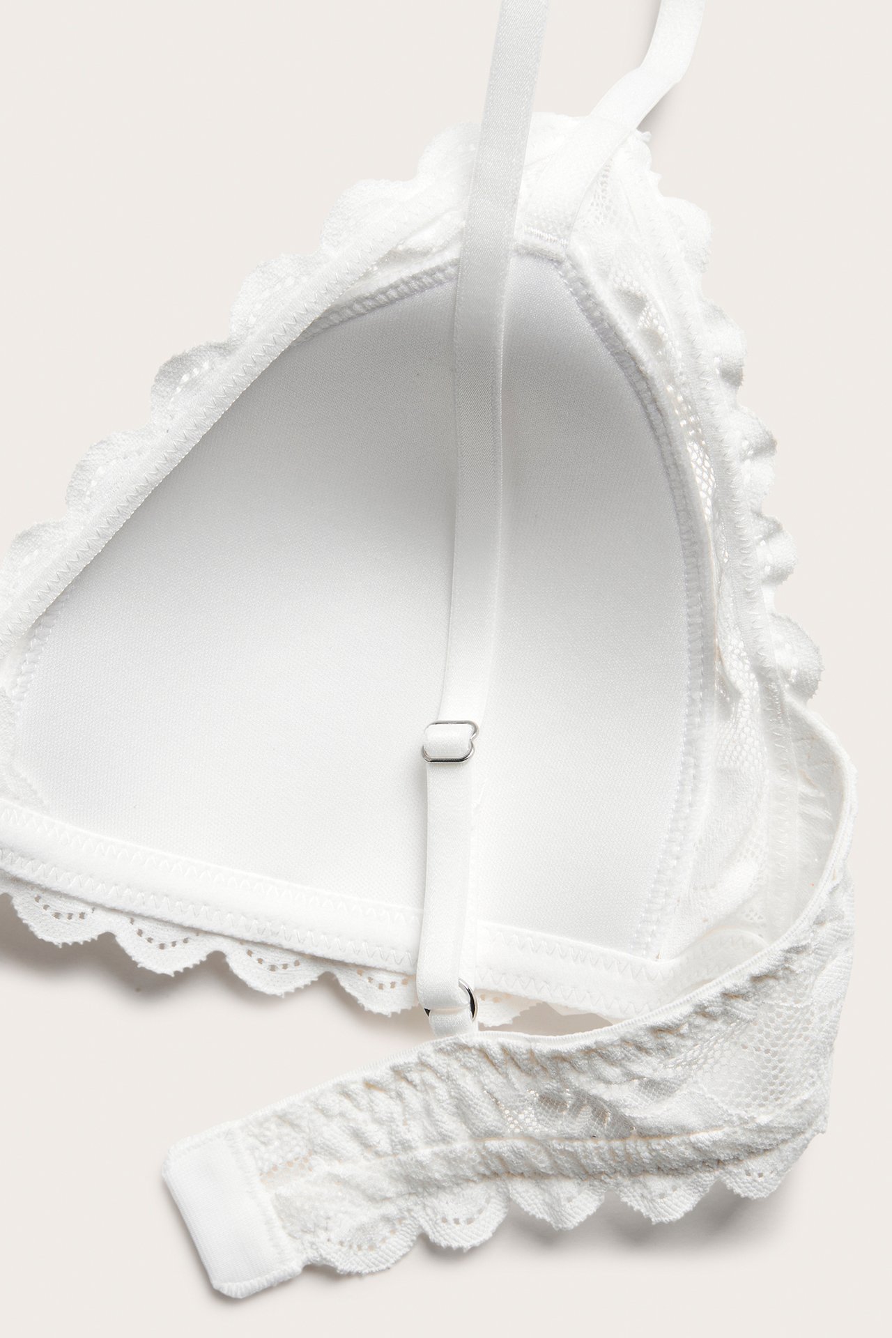 Zbliżenie: off-white koronkowy biustonosz, regulowane ramiączka, stałe wkładki, faliste brzegi.