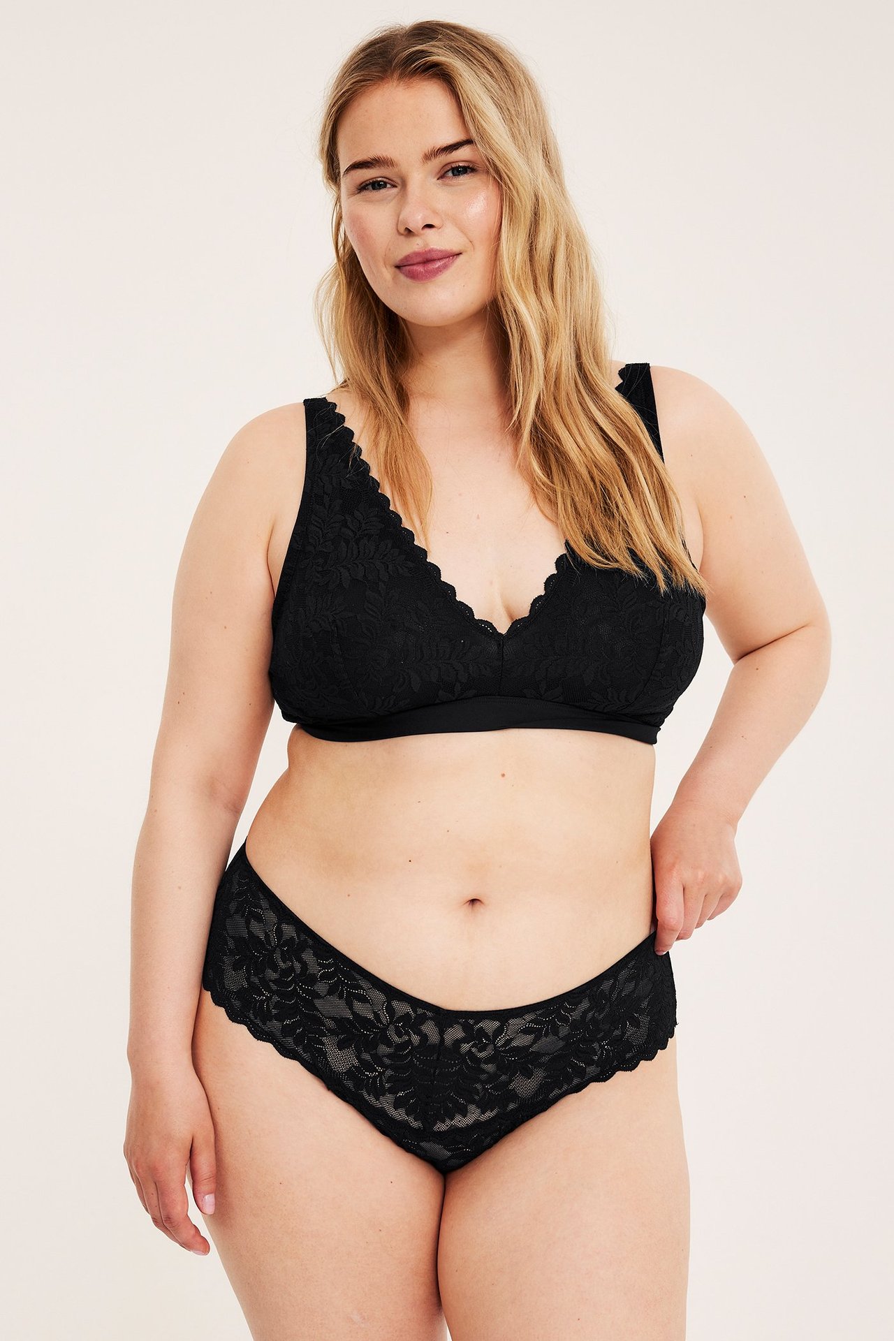 Frontvisning av en kvinne i svarte blonde-cheeky truser med matchende svart blonde-bralette.