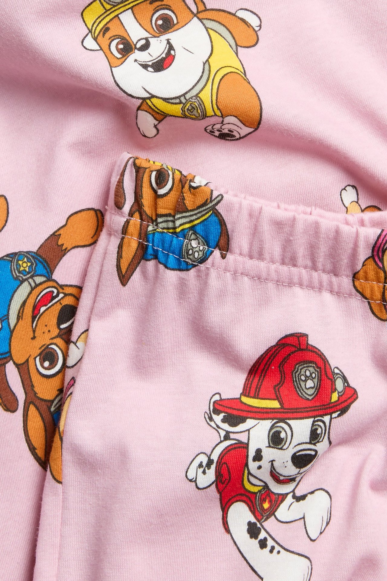 Zbliżenie na jasnoróżową bawełnianą piżamę z kolorowym nadrukiem Psi Patrol.