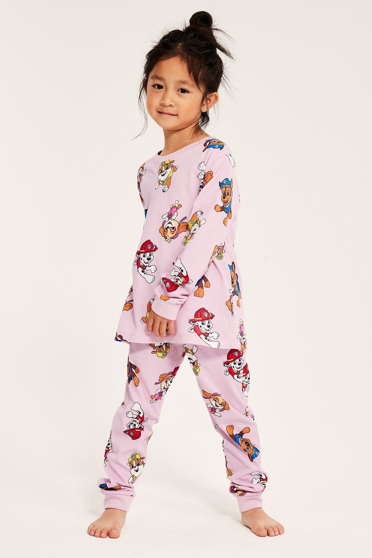 Tyttö in vaaleanpunaiset pyjamat Paw Patrol -kuviolla, pitkähihaiset yläosan ja housut.