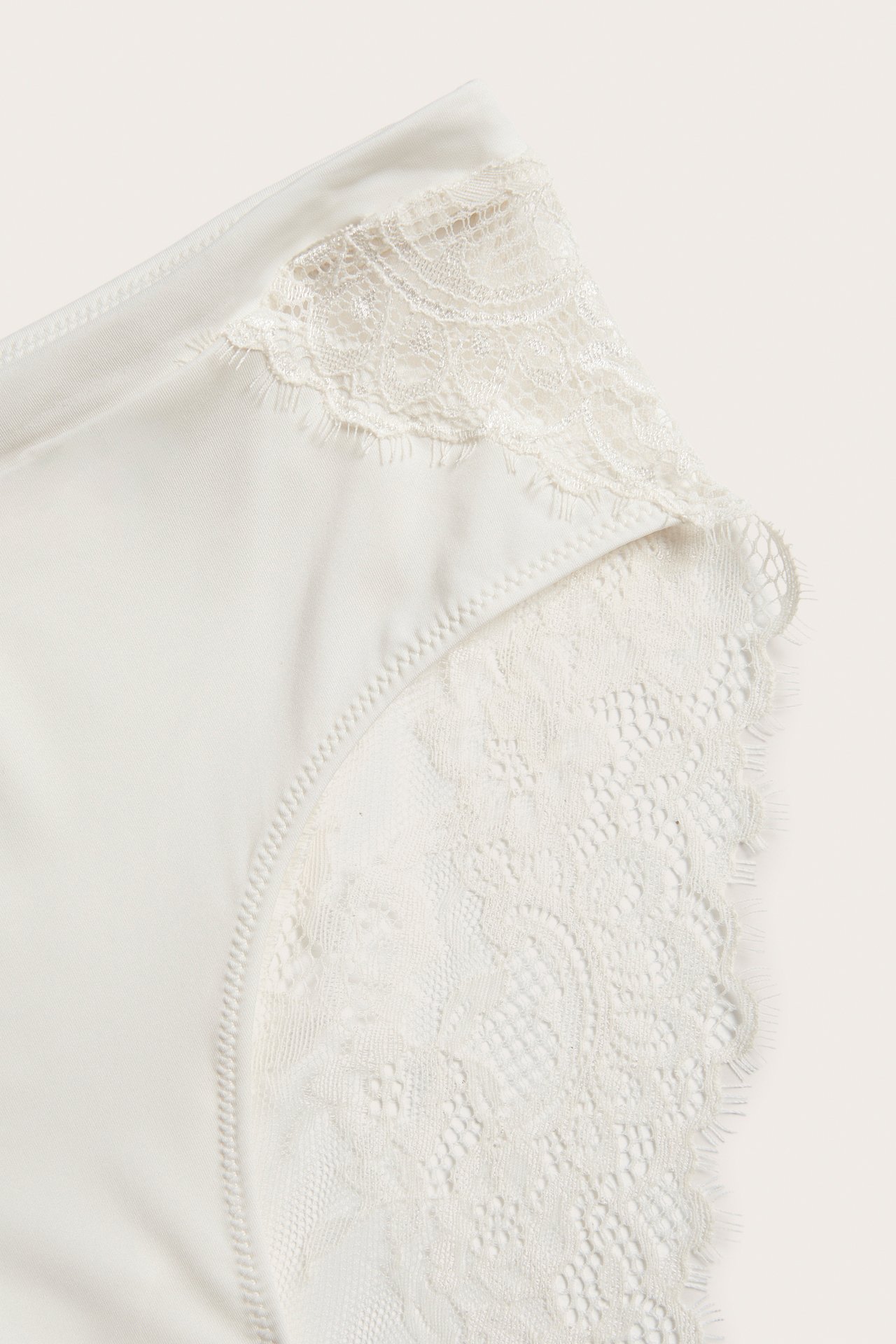 Zbliżenie na majtki z mikrofibry w kolorze ecru z delikatną koronkową lamówką i panelem bocznym.