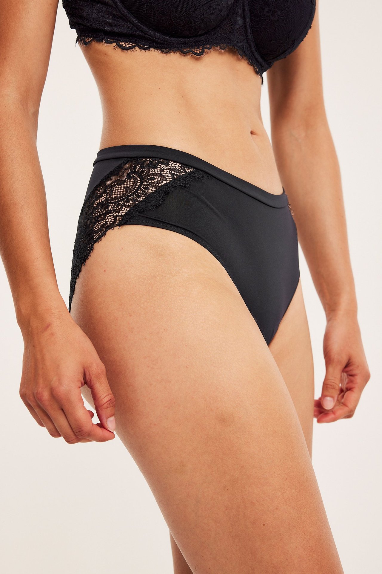 Sidebilde av en kvinne i svarte mikrofiber-briefs med blondedetaljer og en svart blonde-BH.