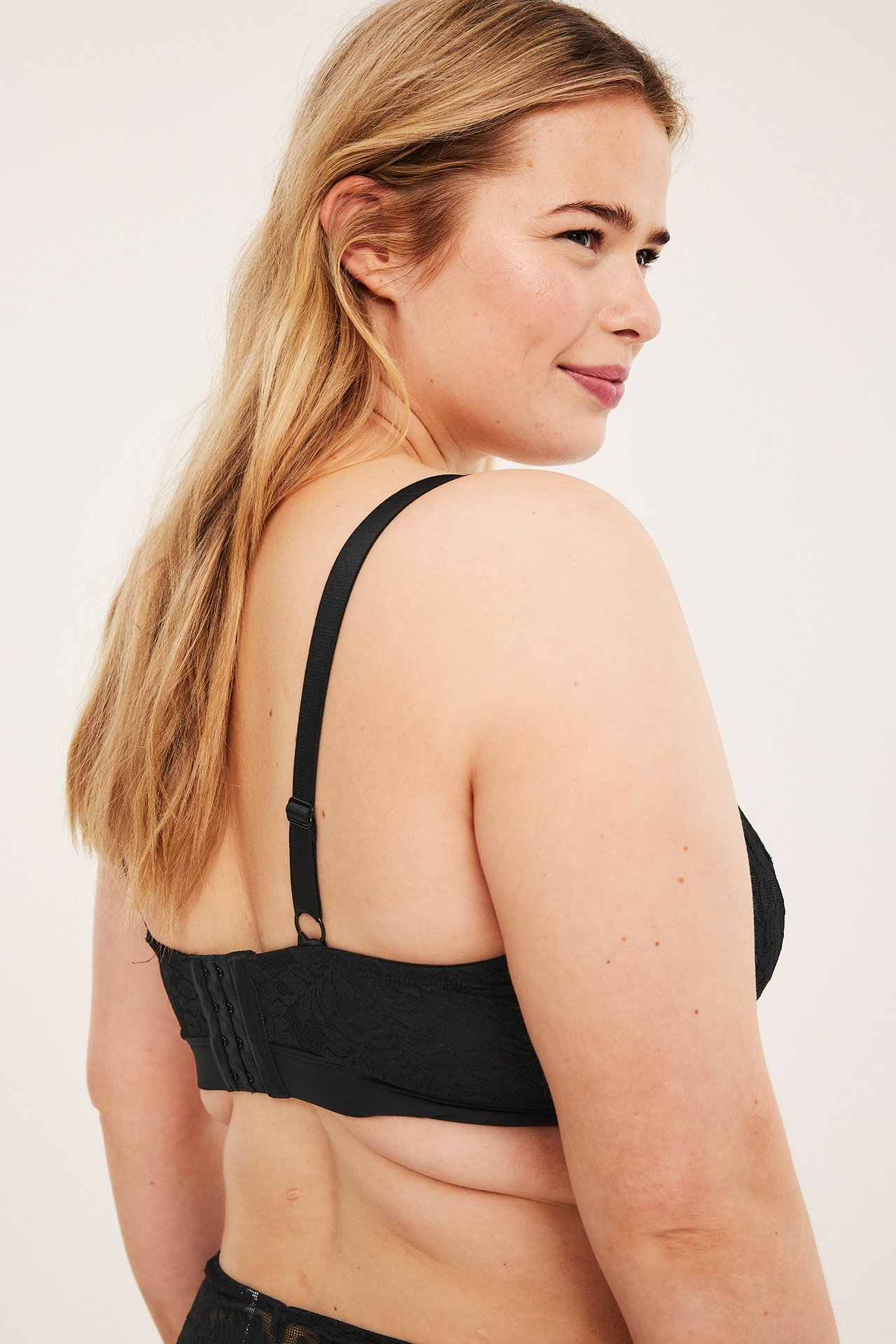 Bakfra-sidevisning av kvinne i svart blondebralette med justerbare stropper og rygglukking.