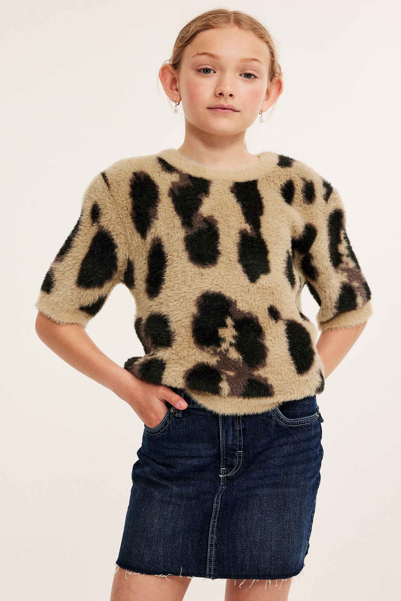 Frontvy av ett barn i en beige och svart leopardmönstrad kortärmad stickad t-shirt och en mörkblå jeanskjol.