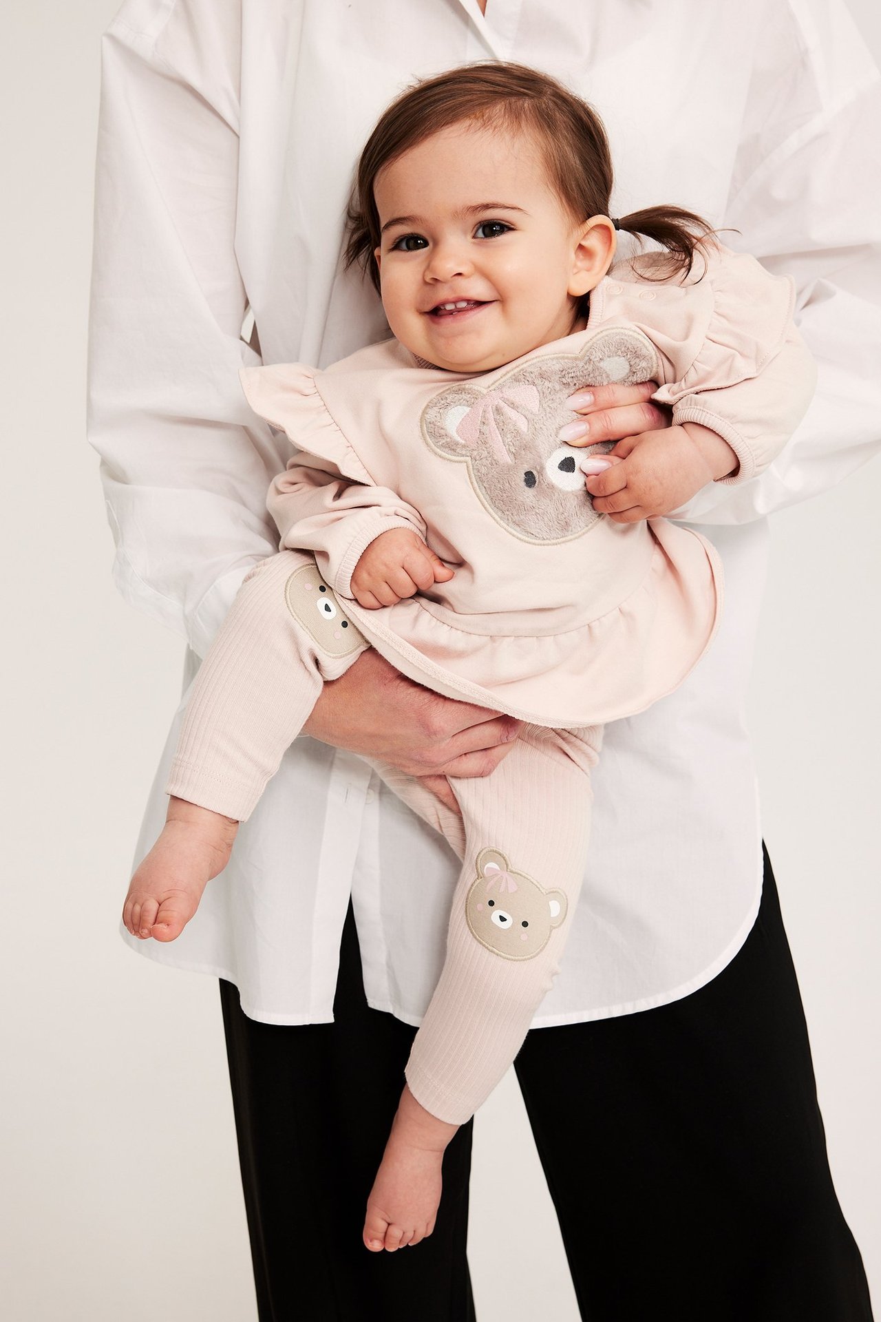 Widok z przodu: niemowlę w różowych prążkowanych legginsach z aplikacjami misia i pasującym różowym topie.