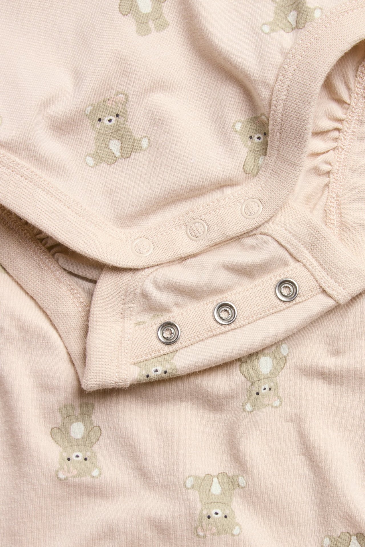 Zbliżenie na różowe body niemowlęce we wzór misia, zapinane na zatrzaski w kroku i na ramieniu.