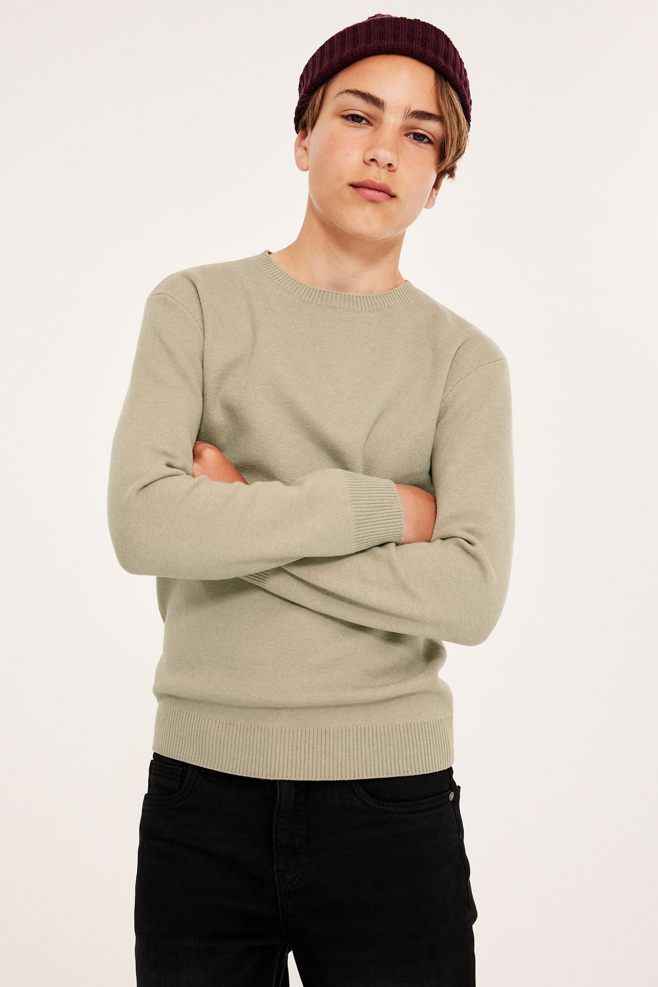 Widok z przodu: dziecko w beżowym dzianinowym swetrze, czarnych dżinsach i bordowej prążkowanej czapce.