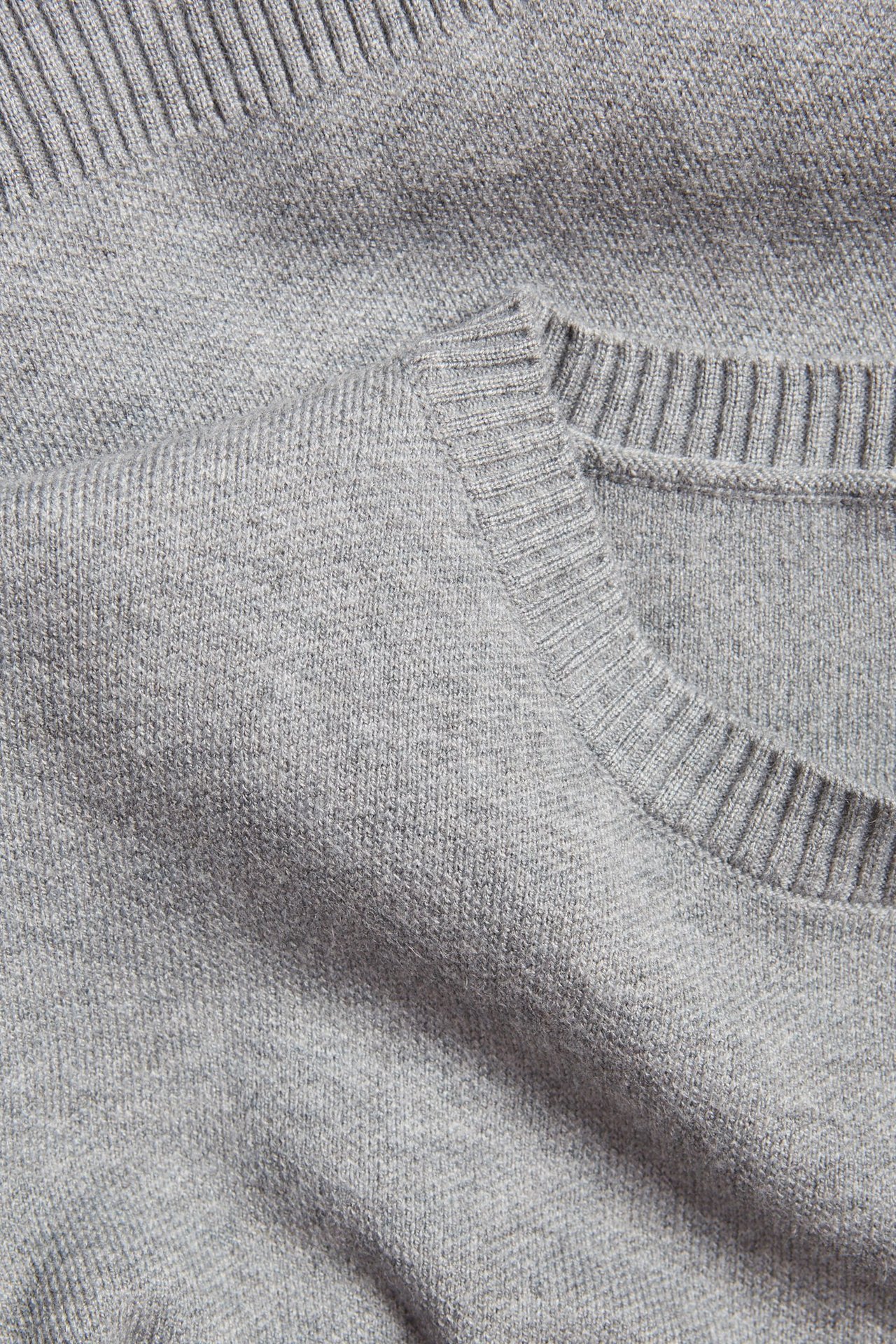 Zbliżenie na ciemnoszary melanżowy sweter z dzianiny z okrągłym dekoltem i prążkowanymi detalami.