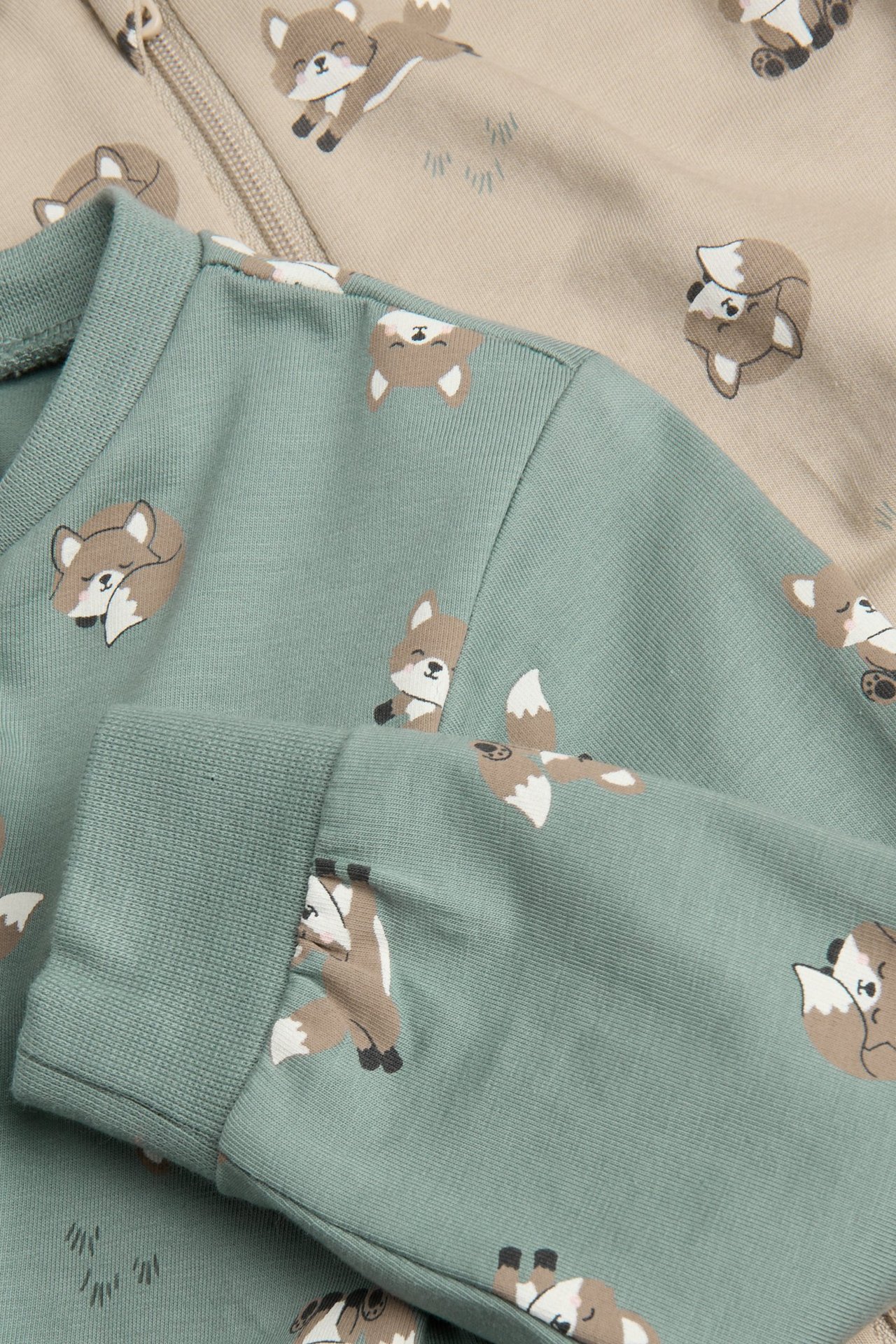 Zbliżenie na jasnozielony pajacyk niemowlęcy w lisy, obok beżowy pajacyk niemowlęcy z zamkiem.