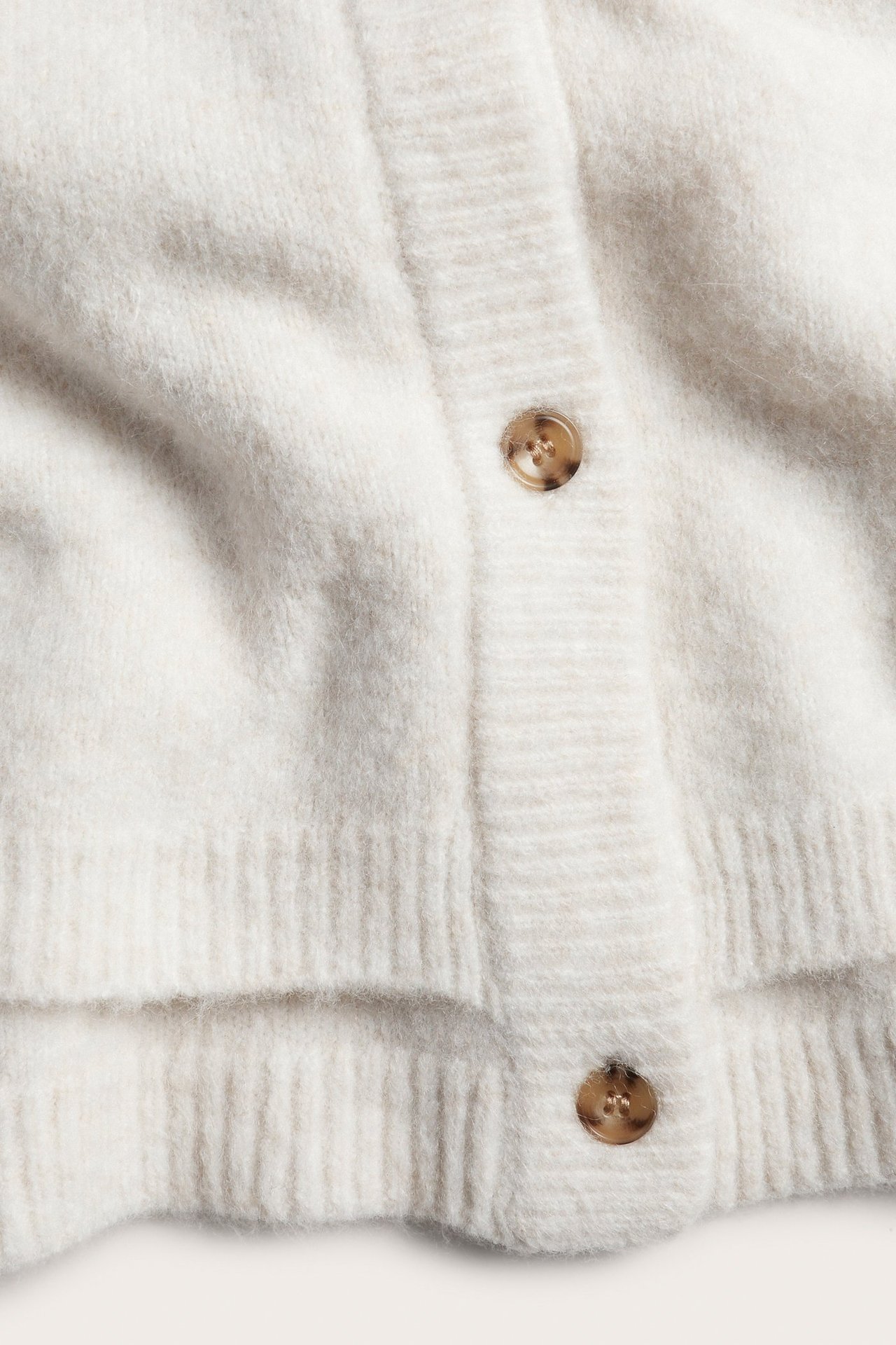 Zbliżenie na białe melanżowe dzianinowe ponczo z brązowymi guzikami z przodu.