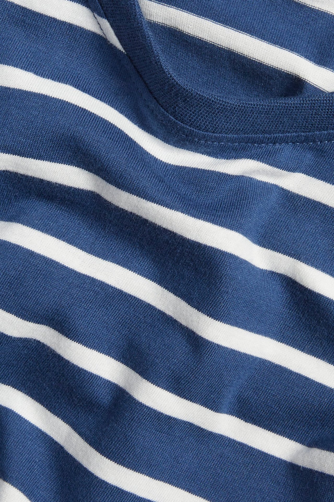 Zbliżenie na granatową i białą pasiastą bawełnianą koszulkę z długim rękawem i prążkowanym dekoltem.