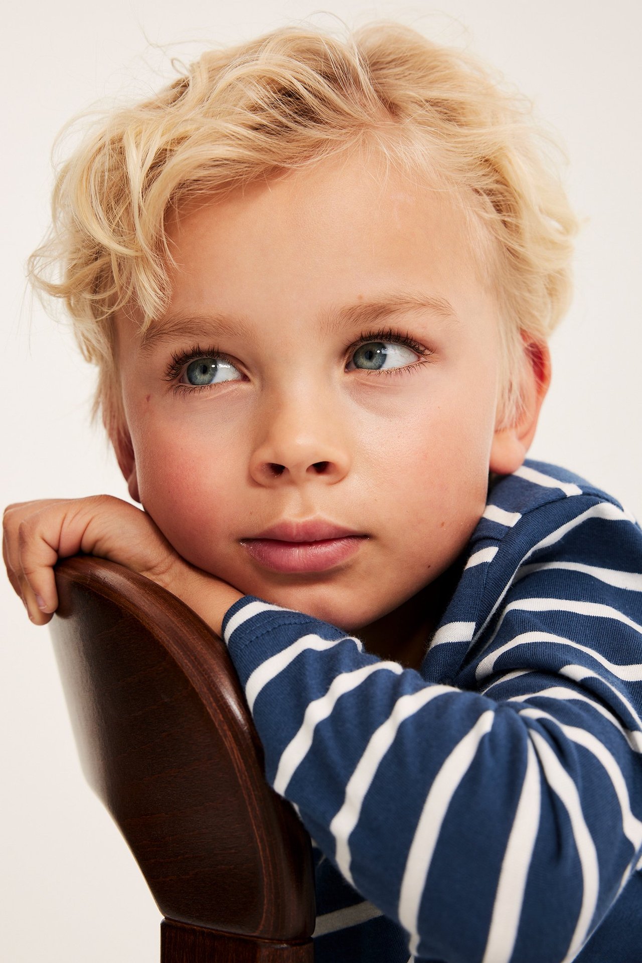 Zbliżenie dziecka w granatowo-białej, pasiastym, długim rękawem bawełnianej koszulce, opierającego się o krzesło.