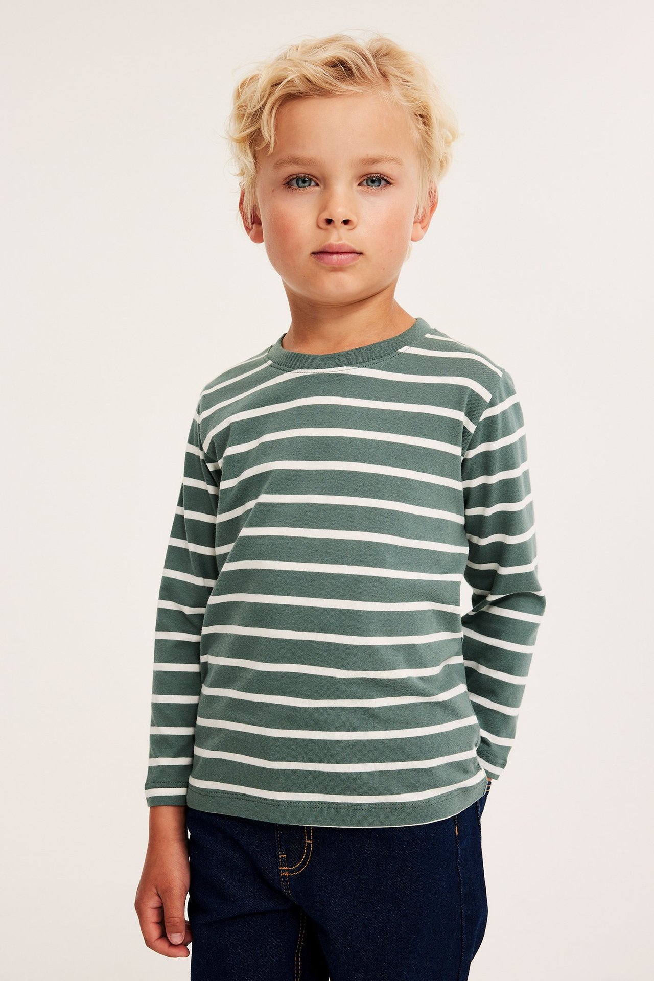 Frontvy av ett barn i en mörkgrön och vitrandig långärmad bomulls-t-shirt och mörkblå jeans.